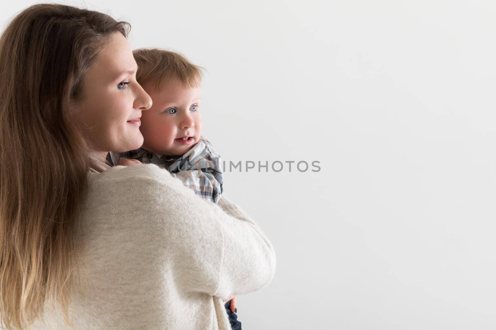 Young european mother with holds a baby in hugs on a white background, both look in one direction, copy space.