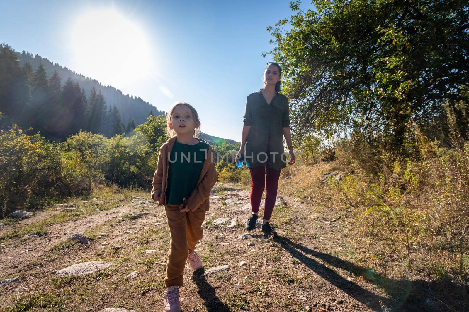 A young mother with her daughter 5 years old on a walk in the mountains. Girl uses a stick like a horse by Rom4ek