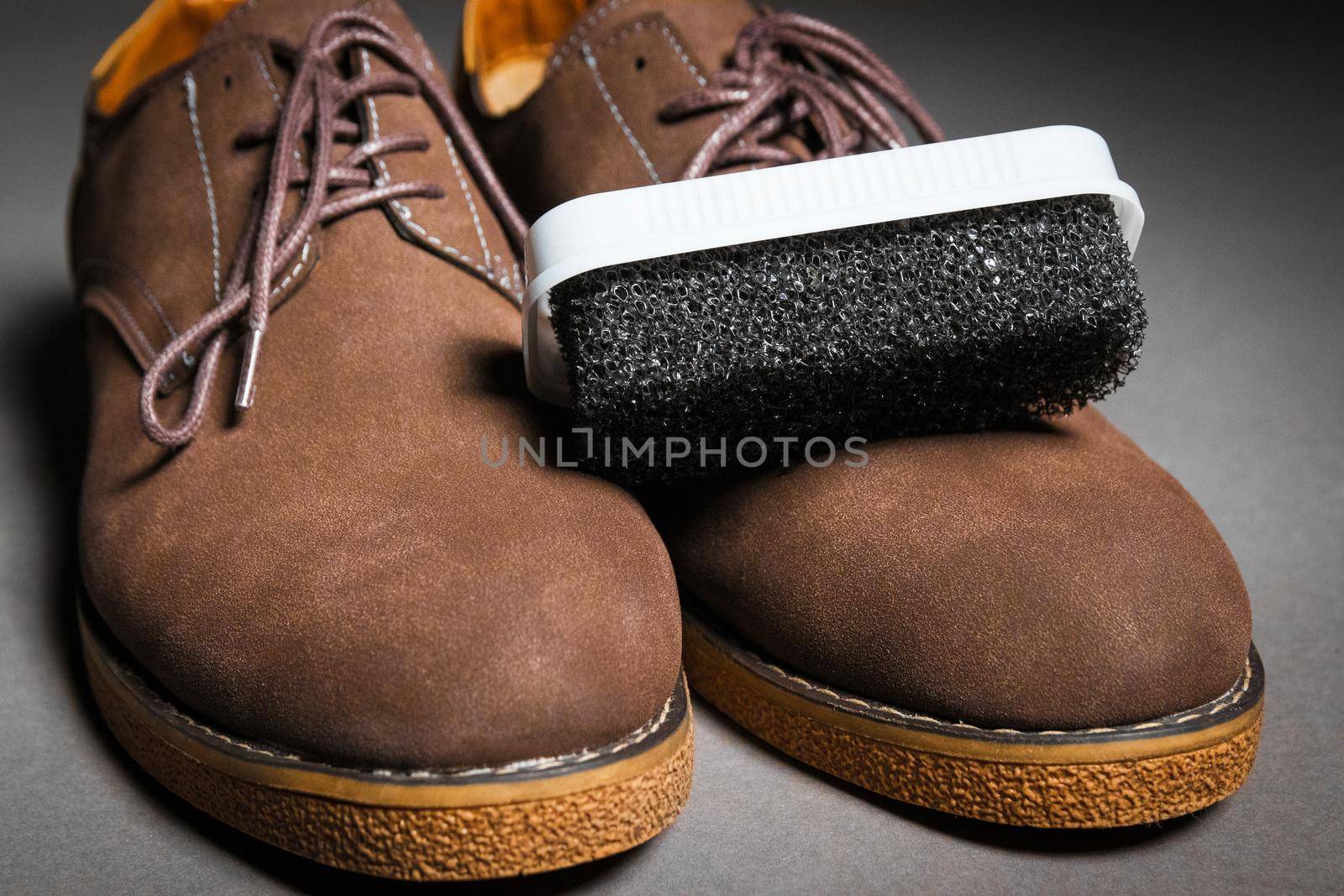 A black sponge for cleaning shoes lies on men's classic brown shoes with laces. Suede shoe care concept.