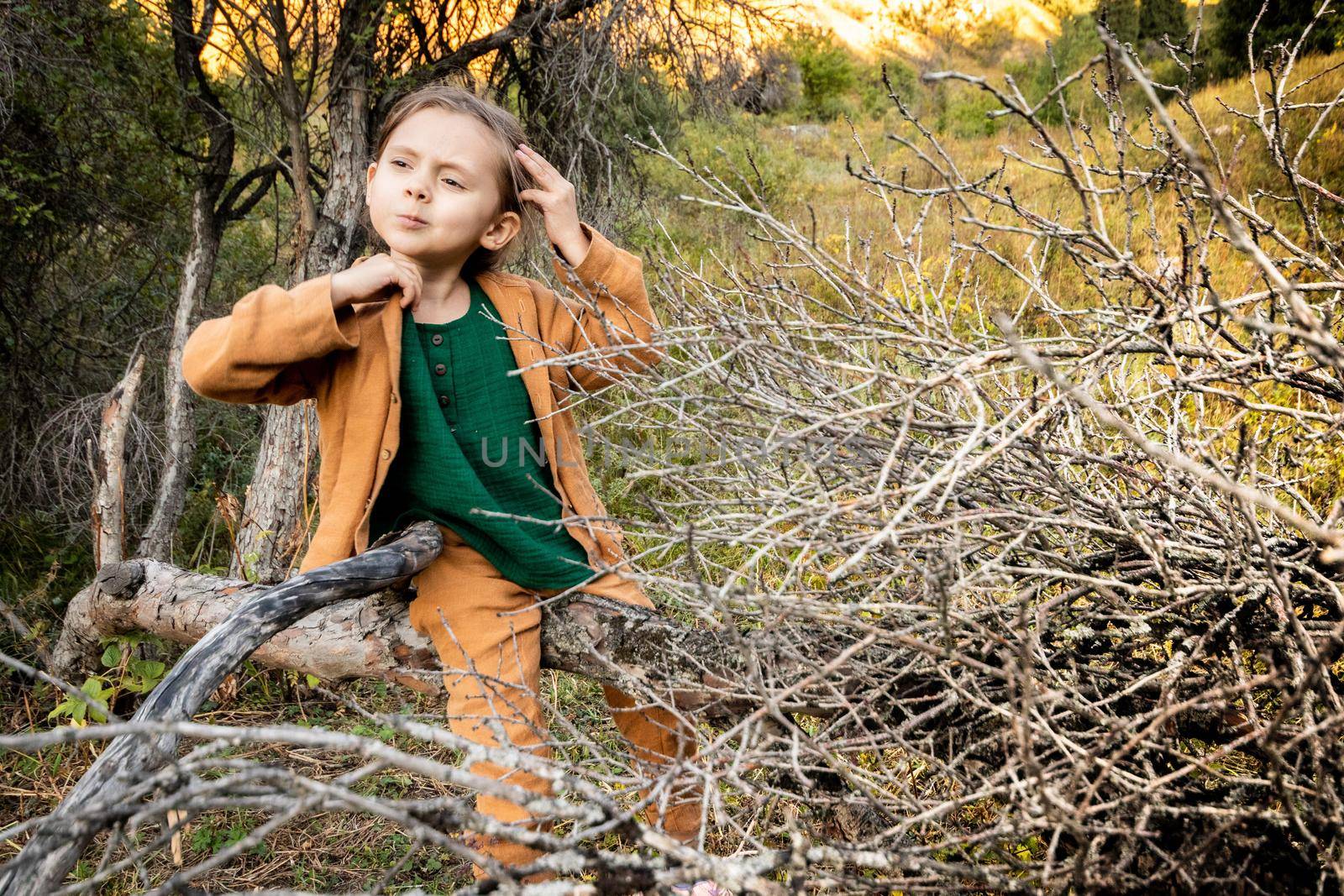 Girl 5 - 7 years old sits on a branch of a fallen tree during outdoor recreation.