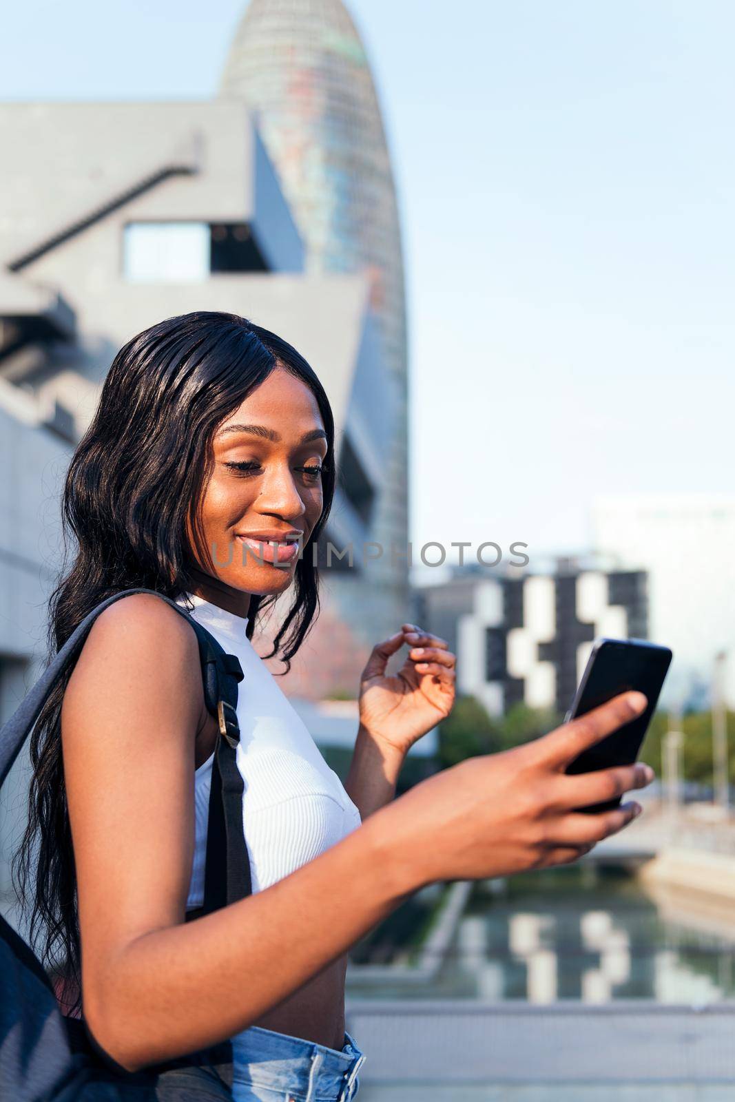 young black girl with backpack smiles consulting her cell phone, concept of youth and urban lifestyle, copy space for text