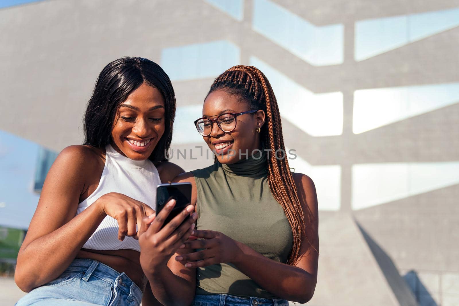 two young black friends smiling and having fun looking at the cell phone, concept of youth and communication technology, copy space for text