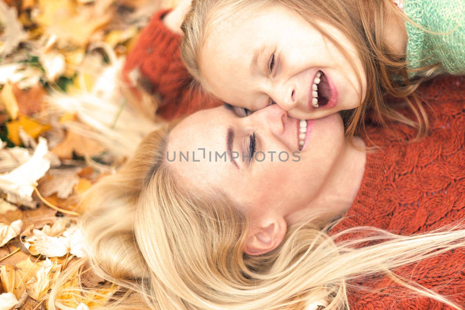 Little girl and young caucasian mom lying down directly above looking at camera on autumn leaves