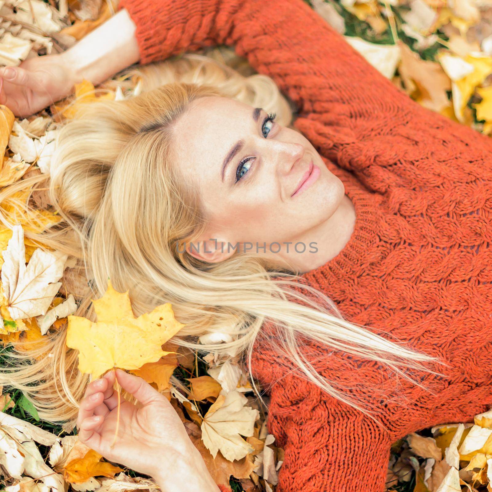 Beautiful young caucasian woman lying down on yellow leaves looking at camera in Autumn Park