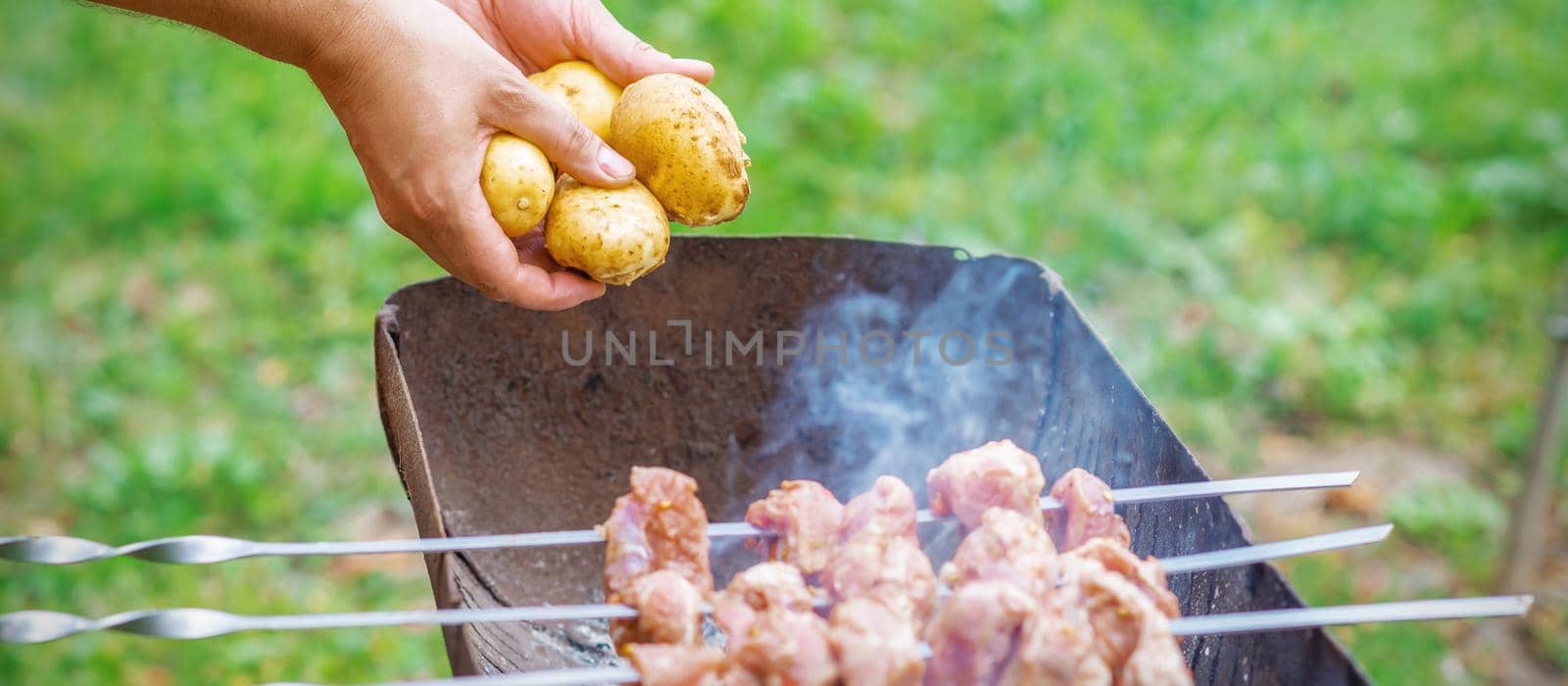 Man prepares barbecue meat with potatoes by okskukuruza