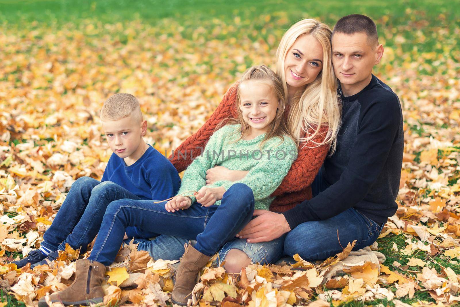 Portrait of young family sitting in autumn leaves. Parents with children sitting in the autumn park