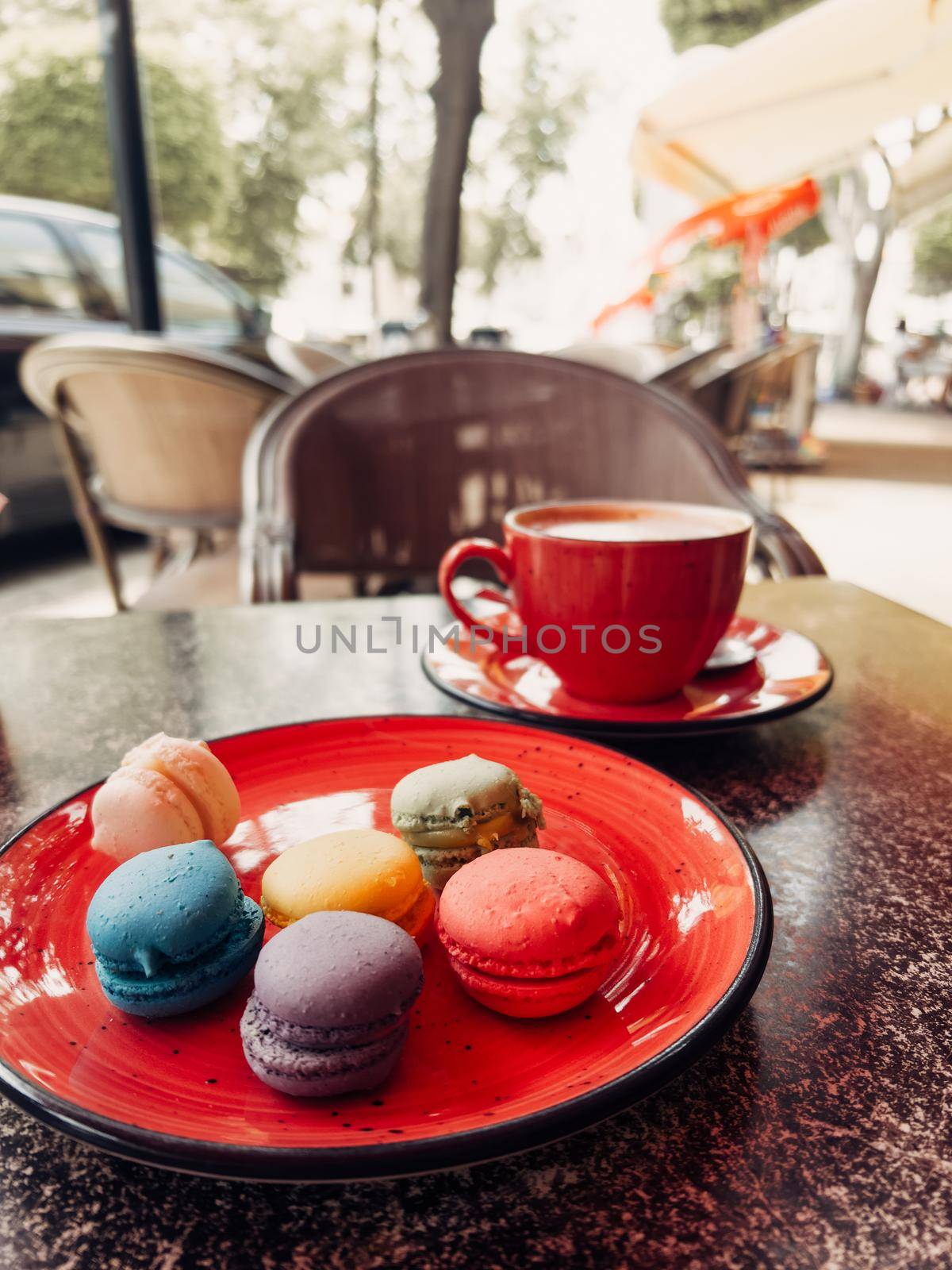 A close up picture of colourful macaron macaroon cakes and coffee mug taken in a street cafe.