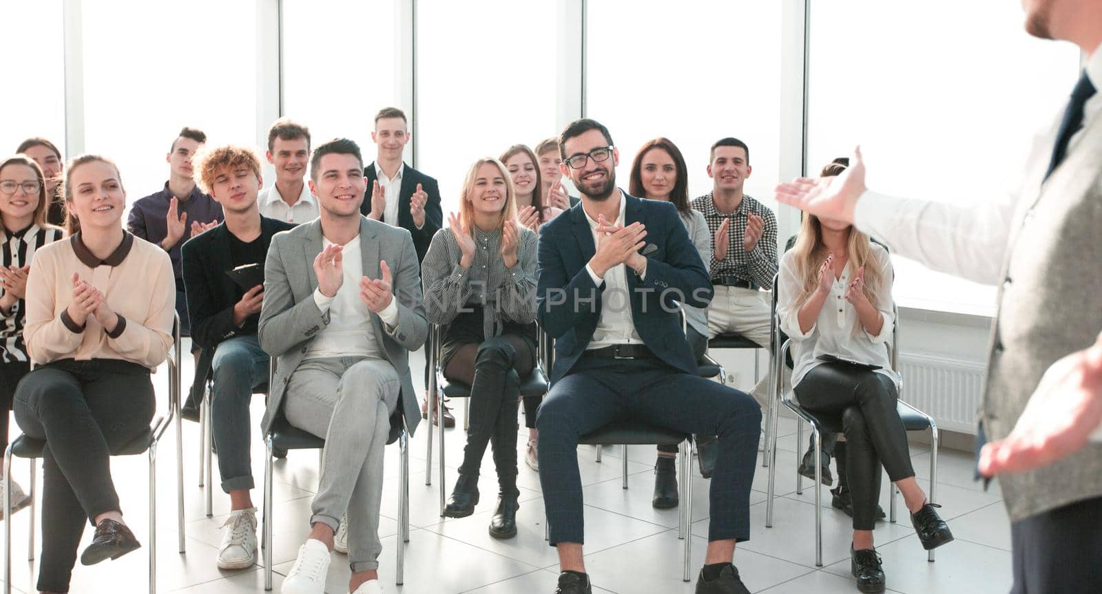 smiling speaker standing in front of an applauding audience . business and education