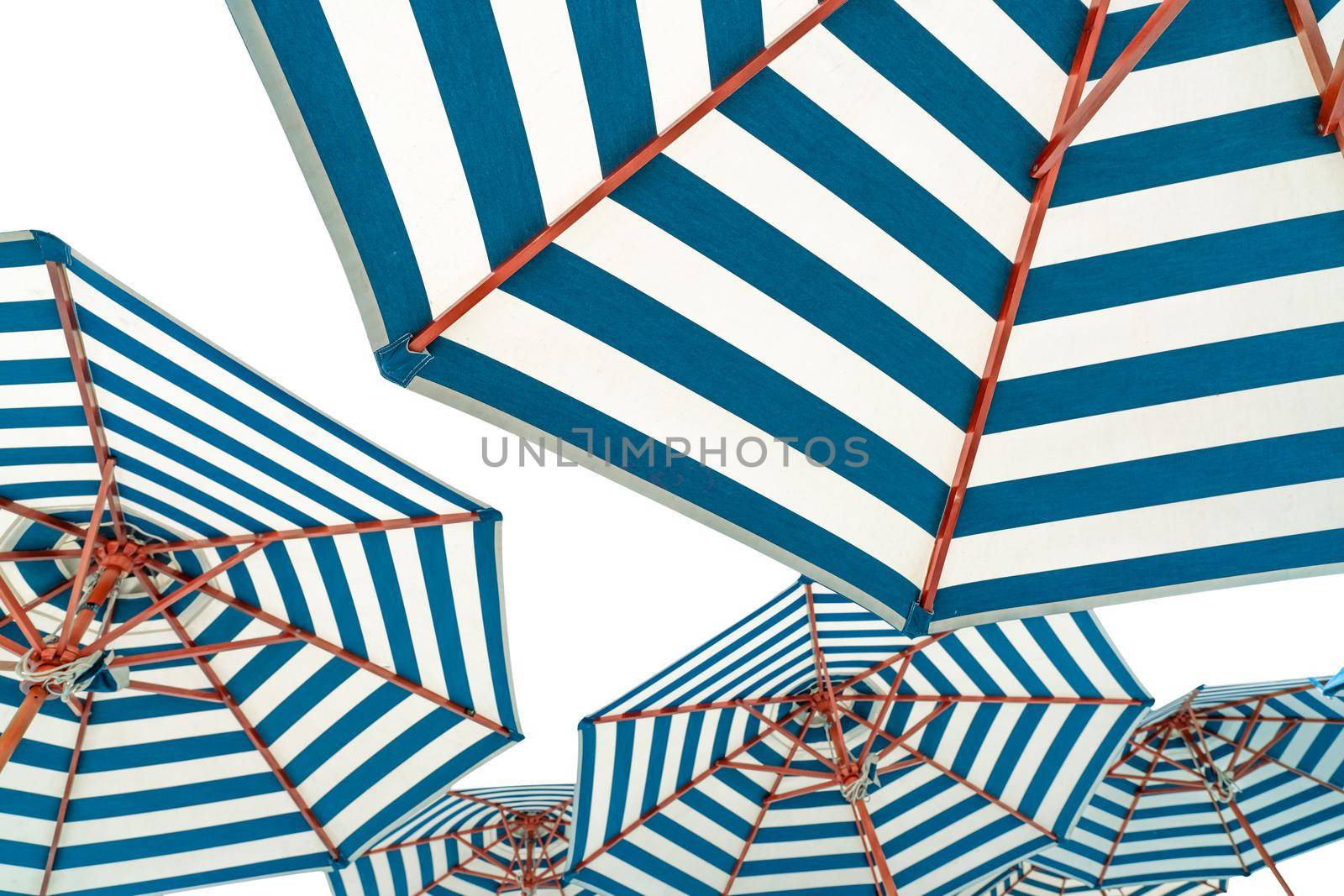 Beach umbrellas isolated on white background. Blue and white striped beach parasol for summer vacation concept. Umbrella for tropical beach in summer. Sunshade for resort decoration. Holiday travel.