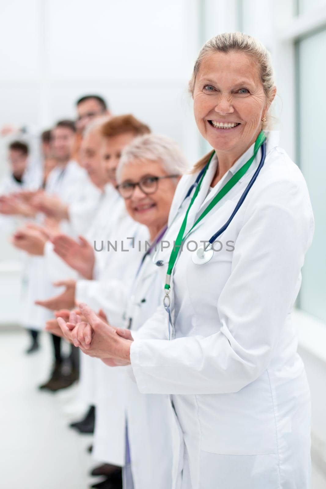 smiling female doctor standing in front of her applauding colleagues. concept of success