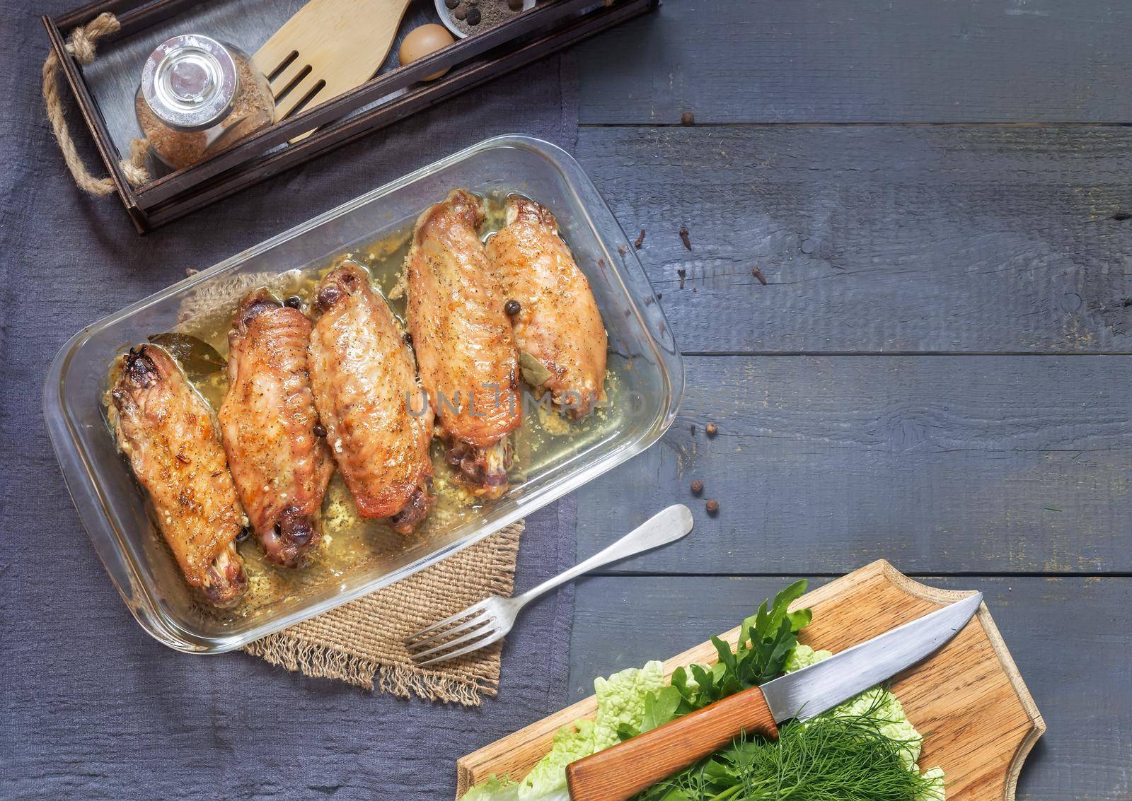 On a wooden table on a napkin is a tray with baked Turkey wings. Next to it are spices and herbs.. Top view, place to copy