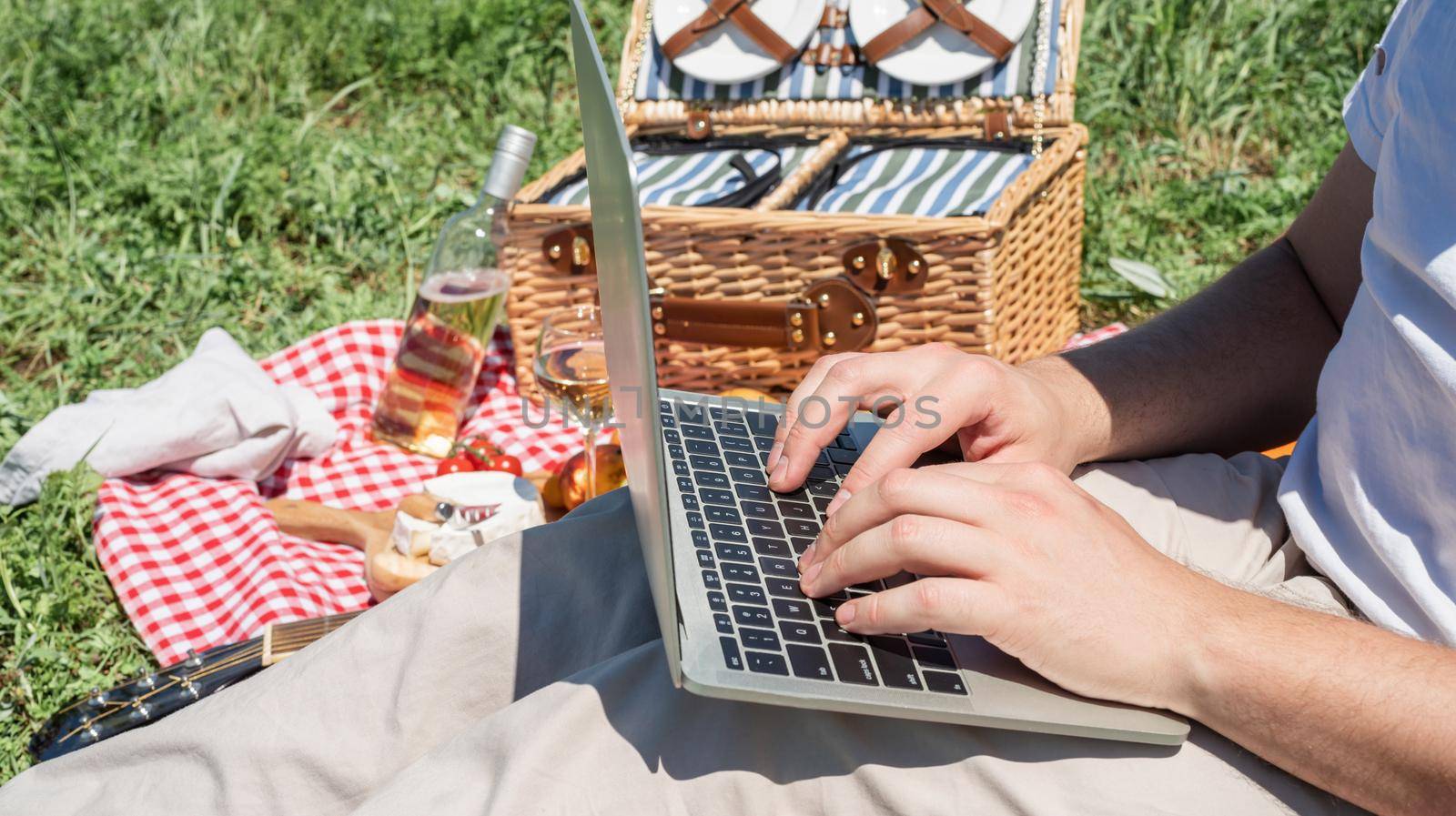 unrecognizable man in white pants outside having picnic and using laptop, working outdoors by Desperada