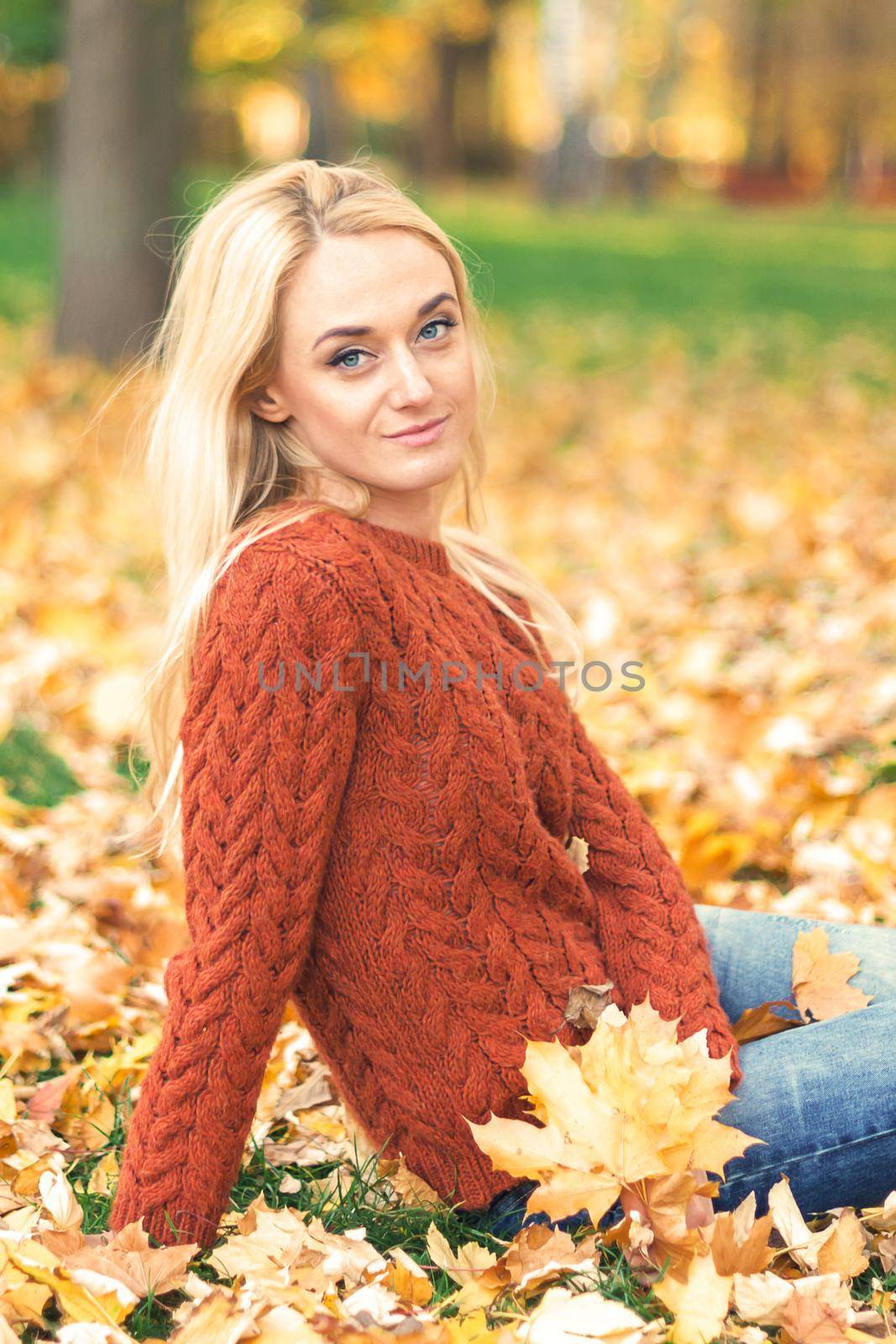 Beautiful young caucasian woman in red sweater sitting on the leaves in the autumn park