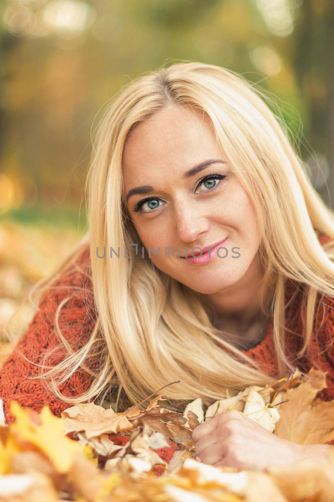 Beautiful young blond hair caucasian woman lies down on leaves at the autumn park