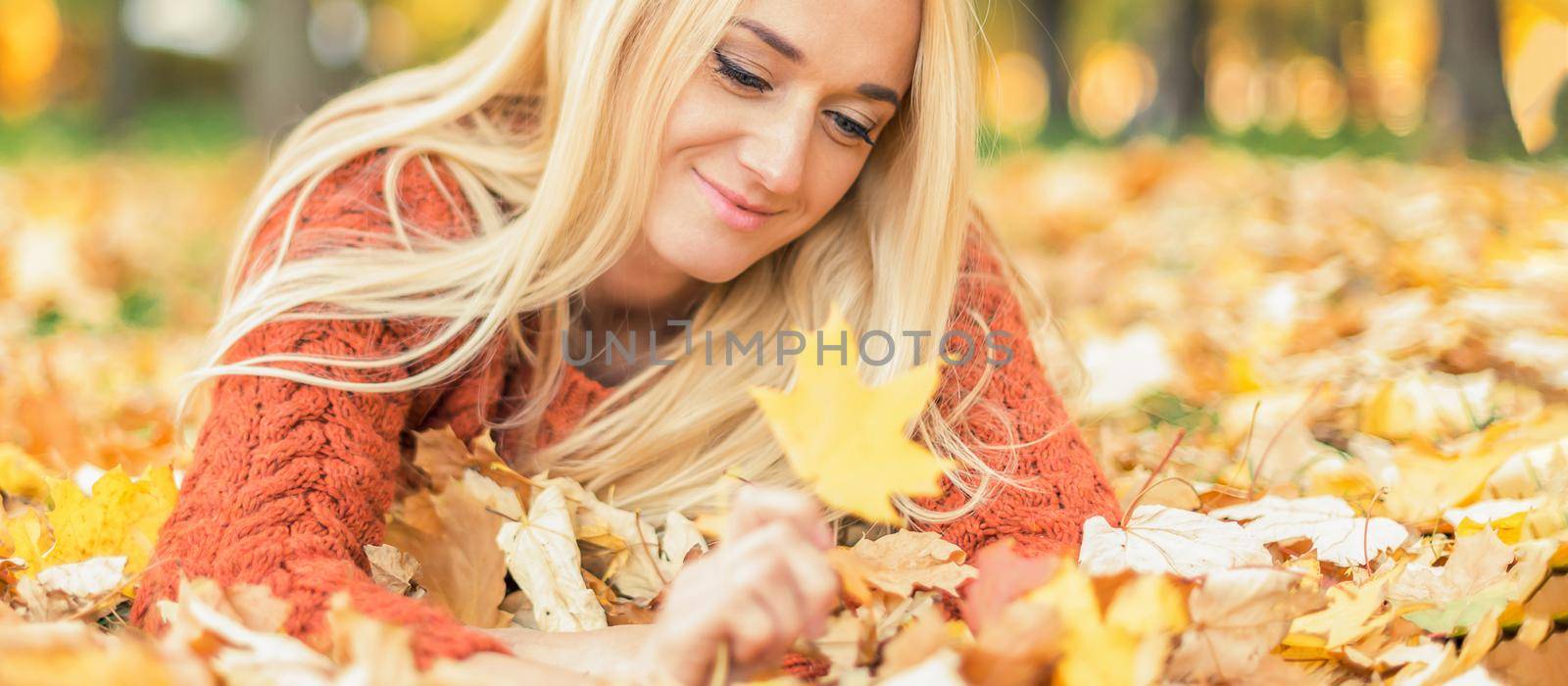 Beautiful young blond hair caucasian woman lies down on leaves at the autumn park