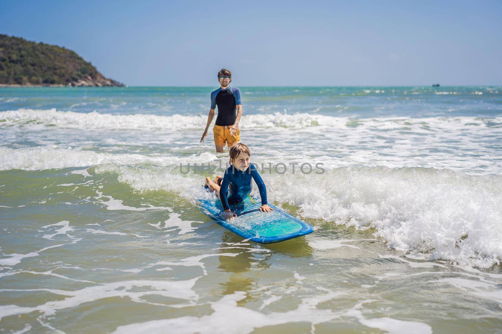 Father or instructor teaching his son how to surf in the sea on vacation or holiday. Travel and sports with children concept. Surfing lesson for kids by galitskaya