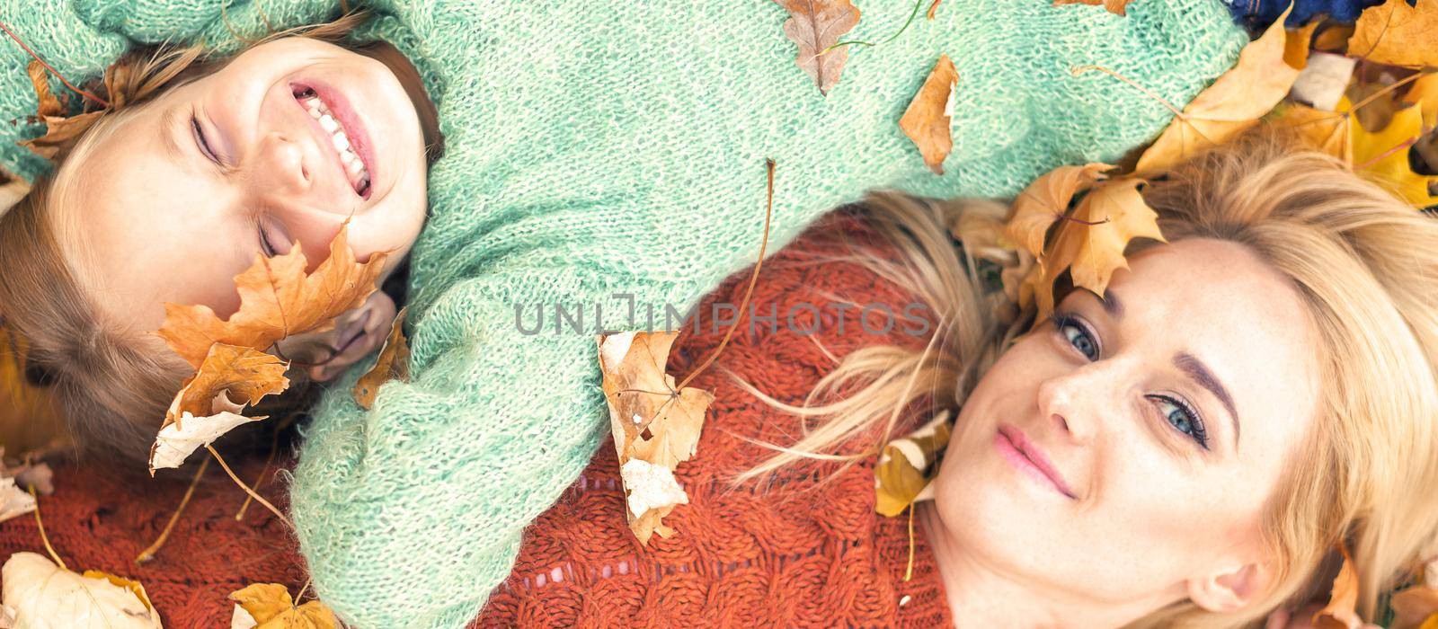 Little girl and young caucasian mom lying down directly above looking at camera on autumn leaves