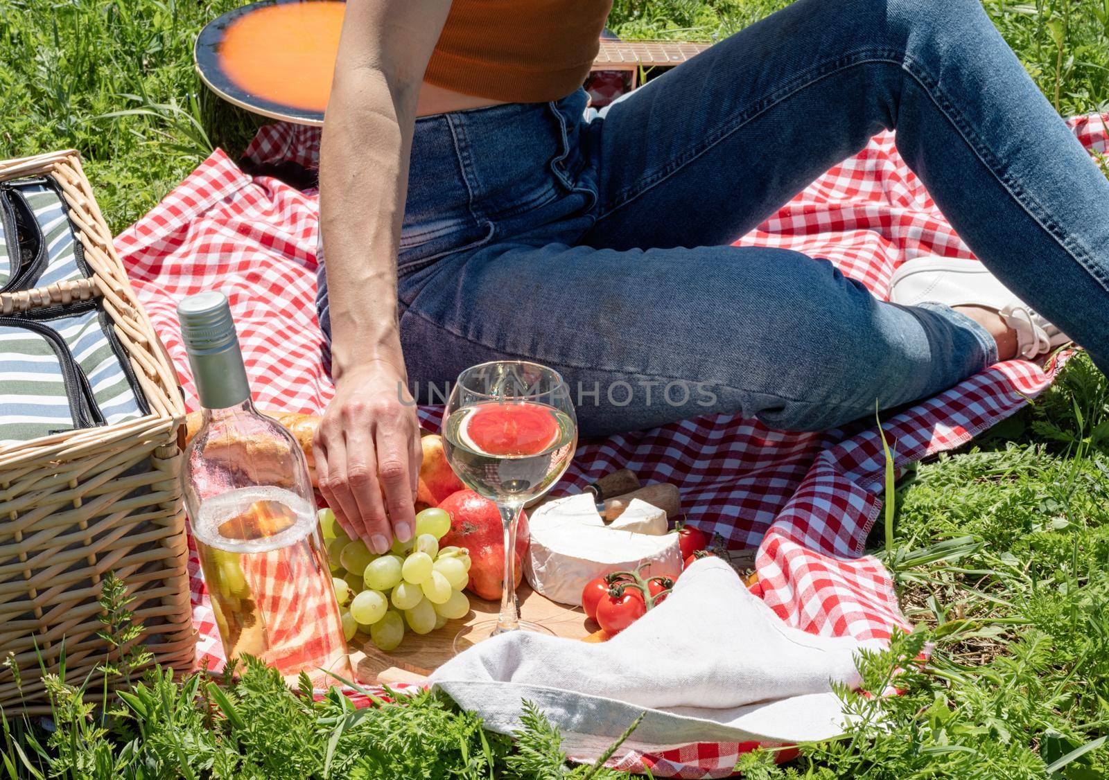 Young woman in park outside at sunny day, enjoying summertime dreaming and drinking wine. Millennial woman having picnic outdoors in sunny day