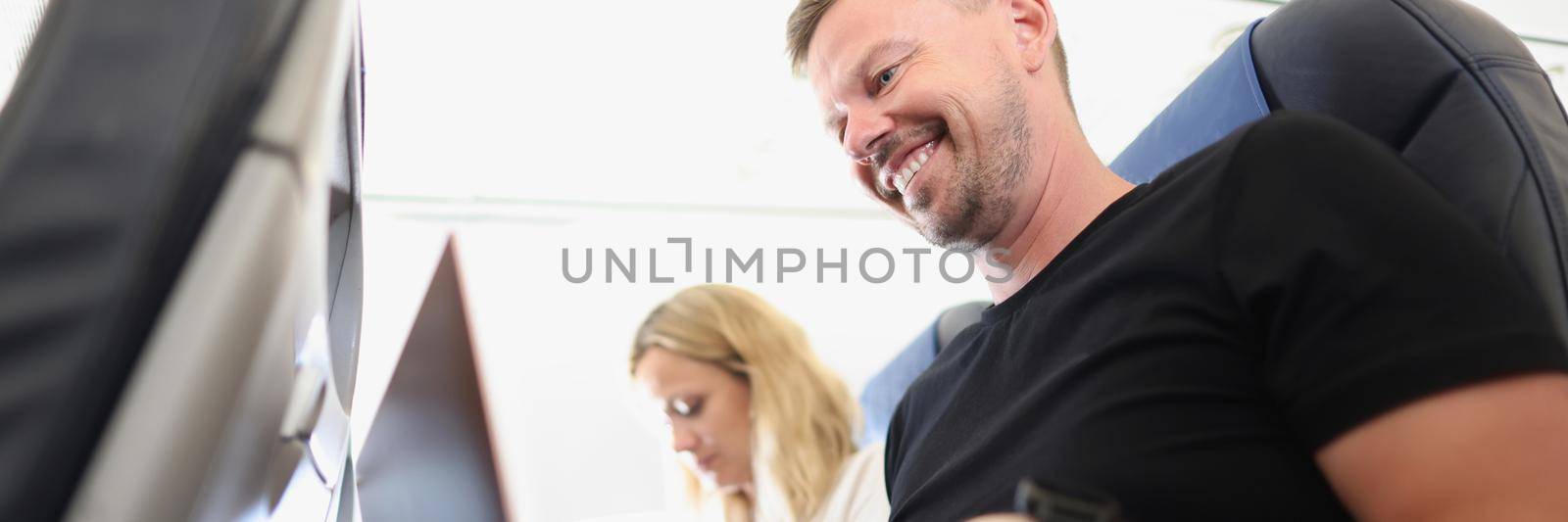Close-up of happy man working on laptop, calm and joyful on airplane trip, woman use smartphone for entertainment. Remote job, freelance, technology, high in sky concept