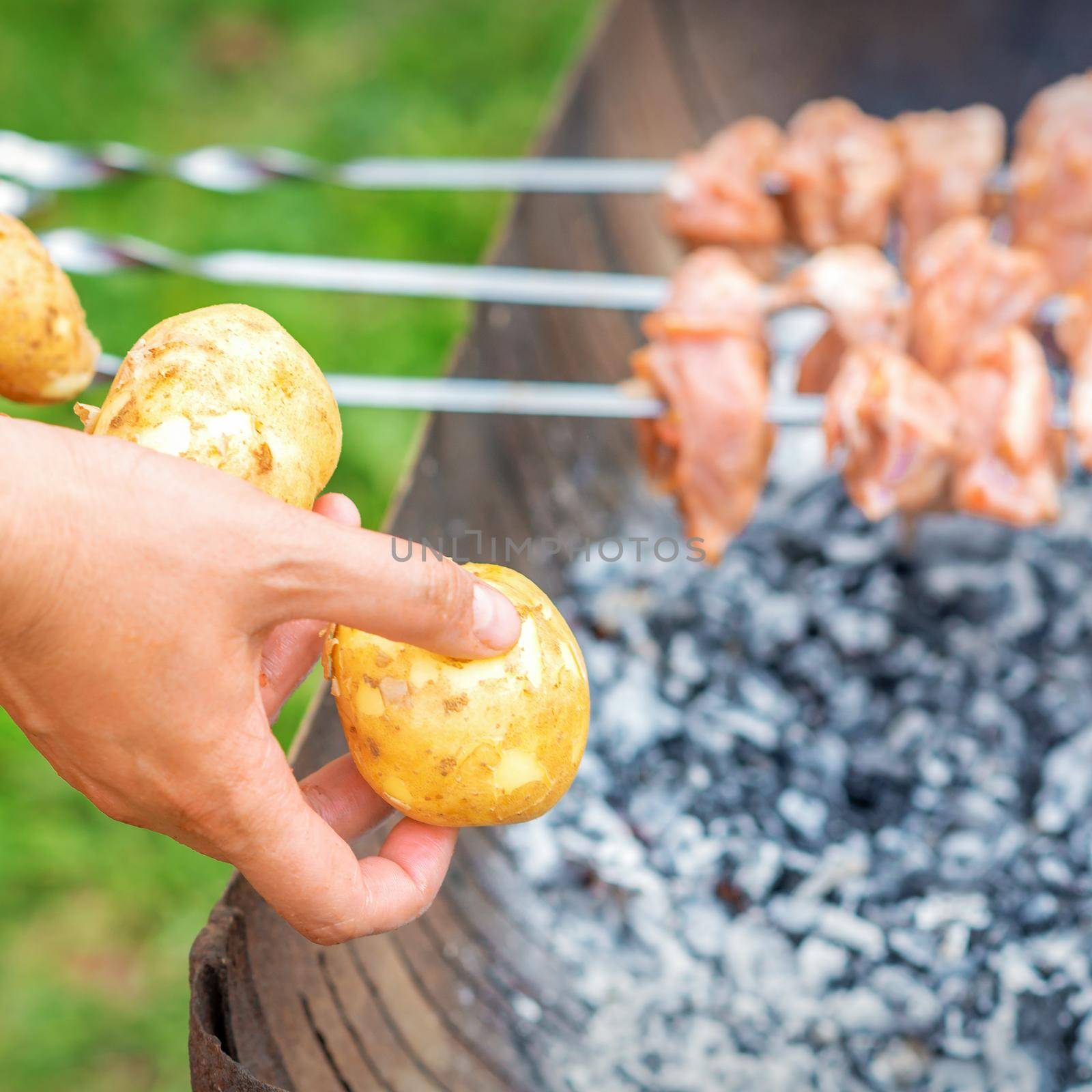 Man prepares barbecue meat with potatoes by okskukuruza