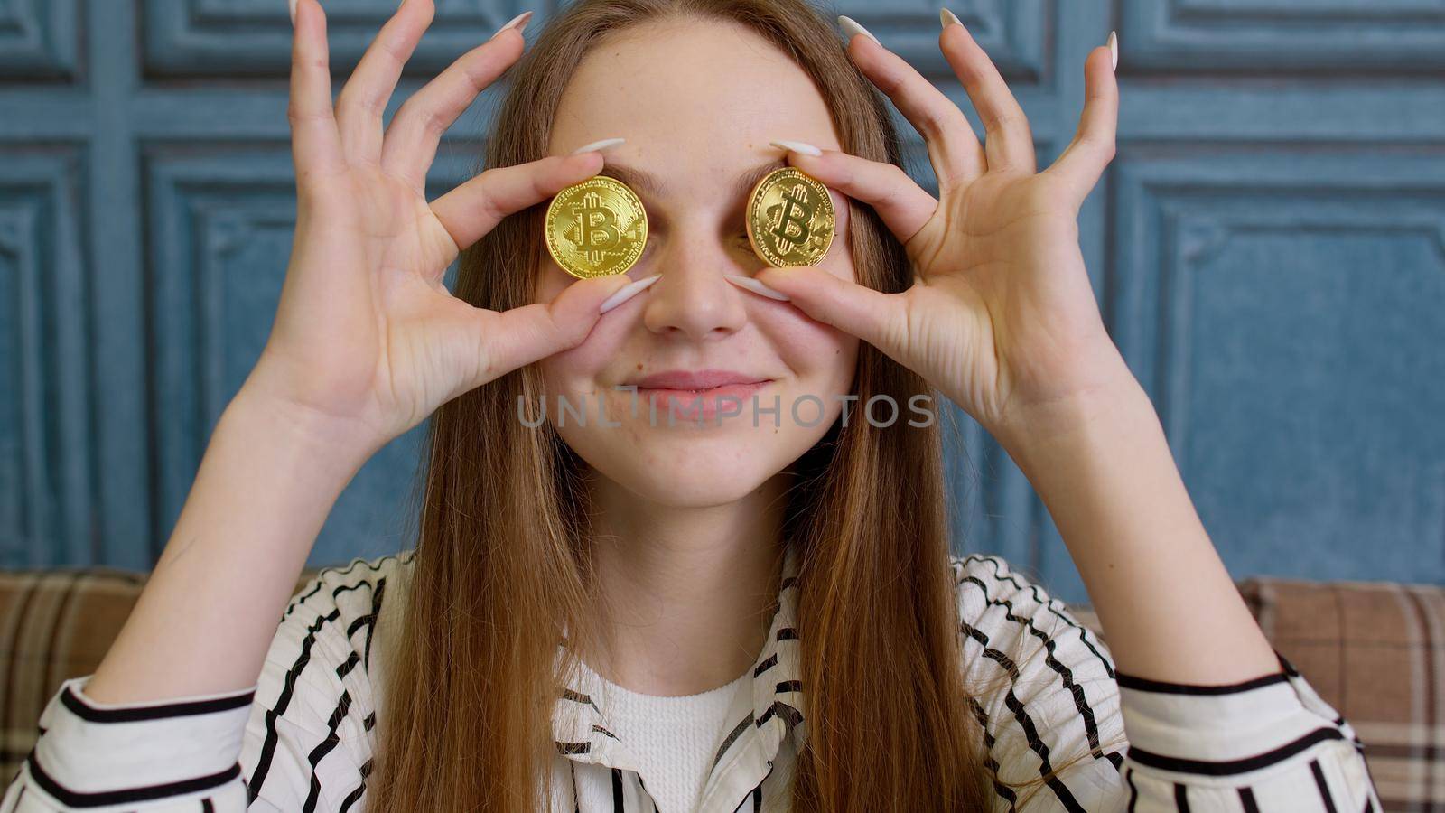 Woman freelancer holding two gold coins at home, successful developer programmer. Girl stock trader earning bitcoins after online monitoring trading operations. Increasing wealth, financial prosperity