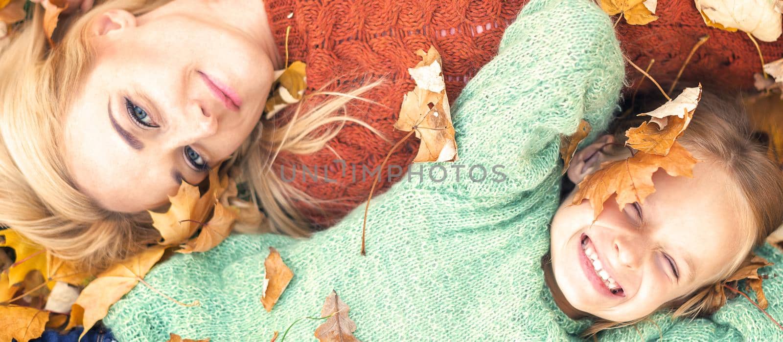 Little girl and young caucasian mom lying down directly above looking at camera on autumn leaves