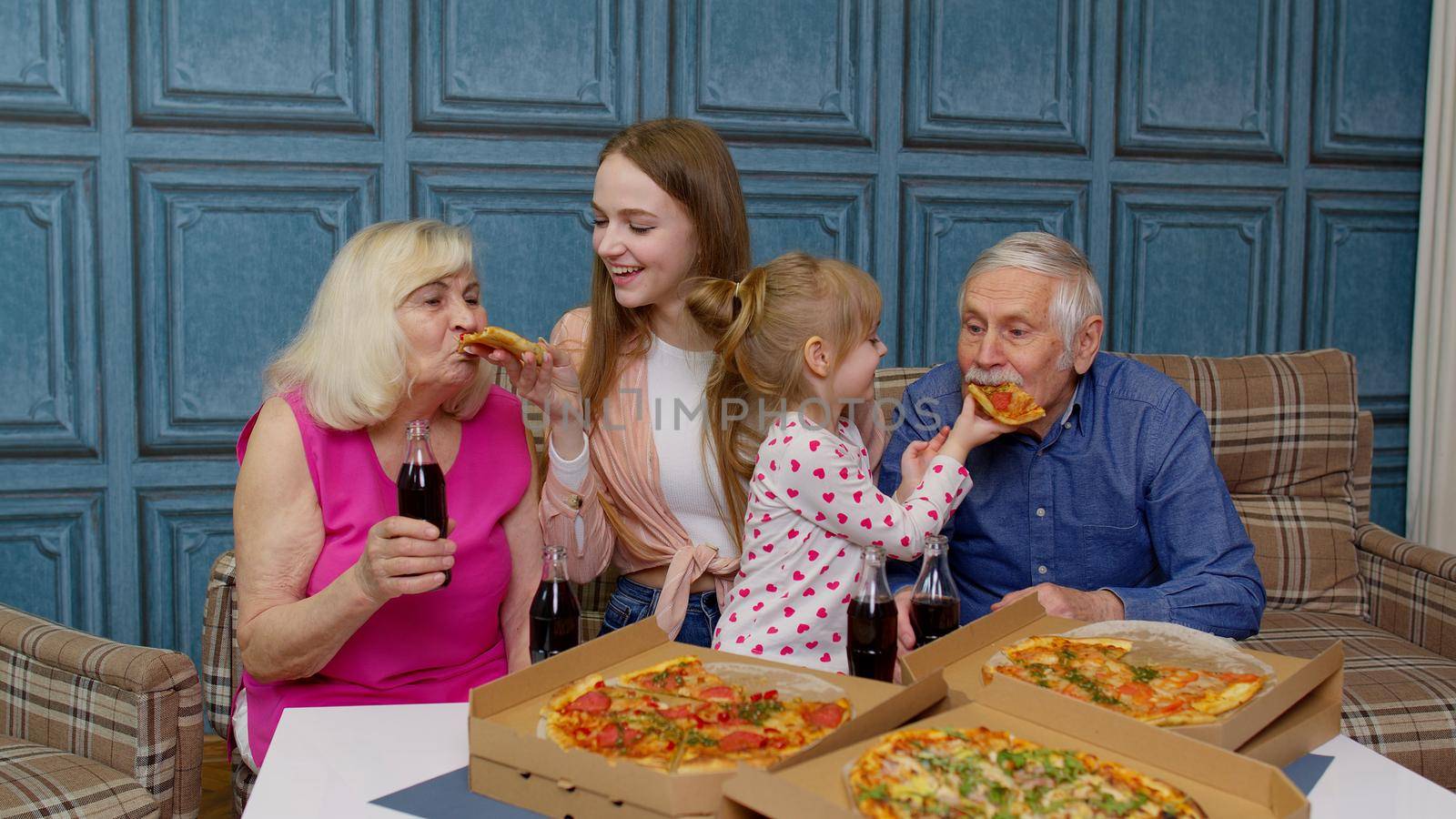 Multigenerational family having lunch party, feed each other with pizza, laughing, enjoying meal together at home. Grandparents with young woman and child. Celebration holidays, weekends, birthday