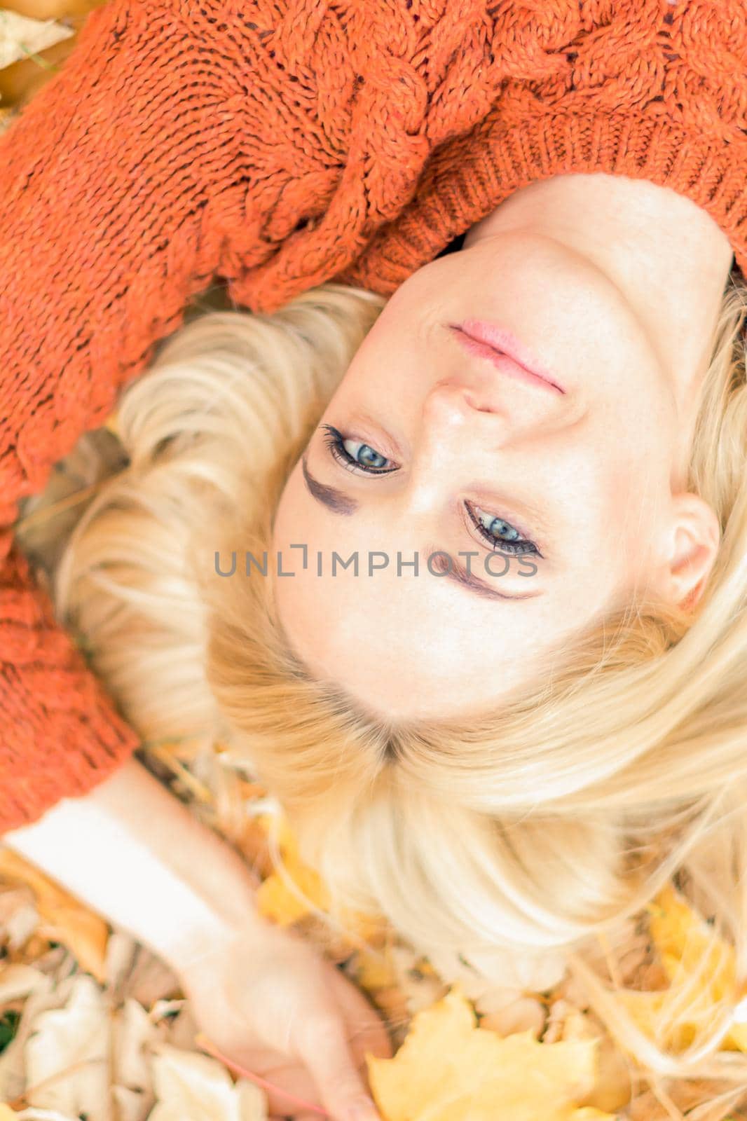 Beautiful young caucasian woman lying down on yellow leaves looking at camera in Autumn Park