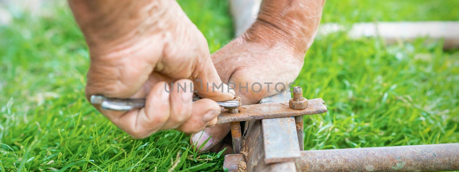 hand of an elderly man twisting the nut with a wrench outdoors. Repair by wrench.