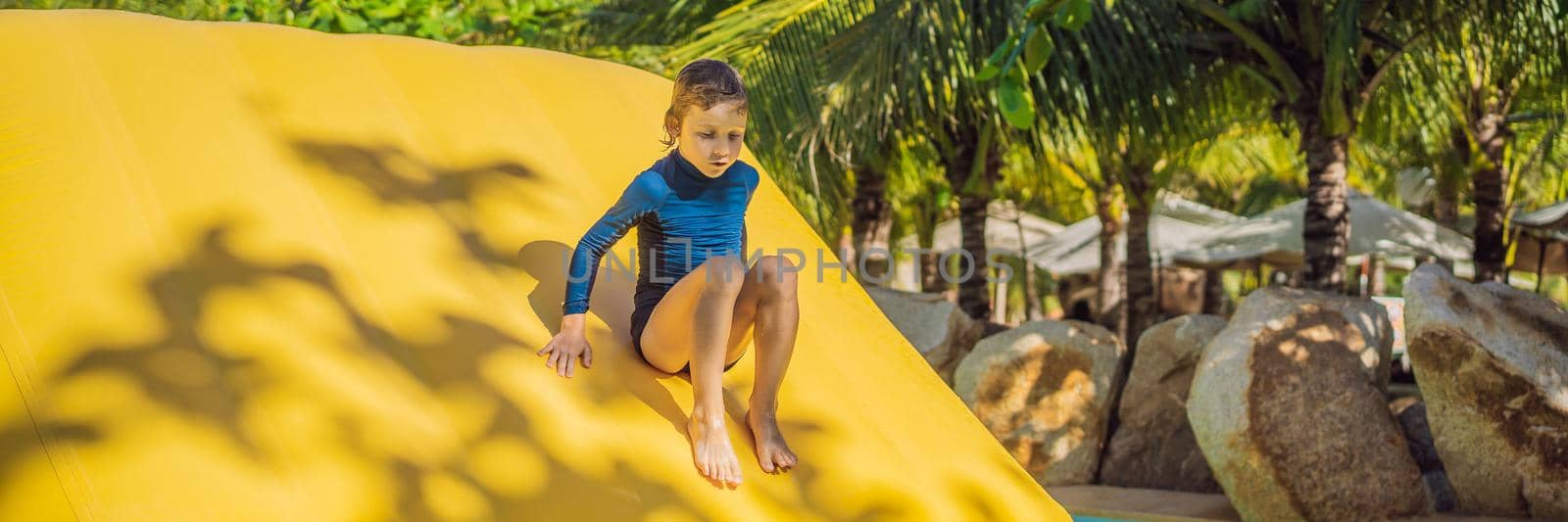 Cute boy runs an inflatable obstacle course in the pool. BANNER, LONG FORMAT