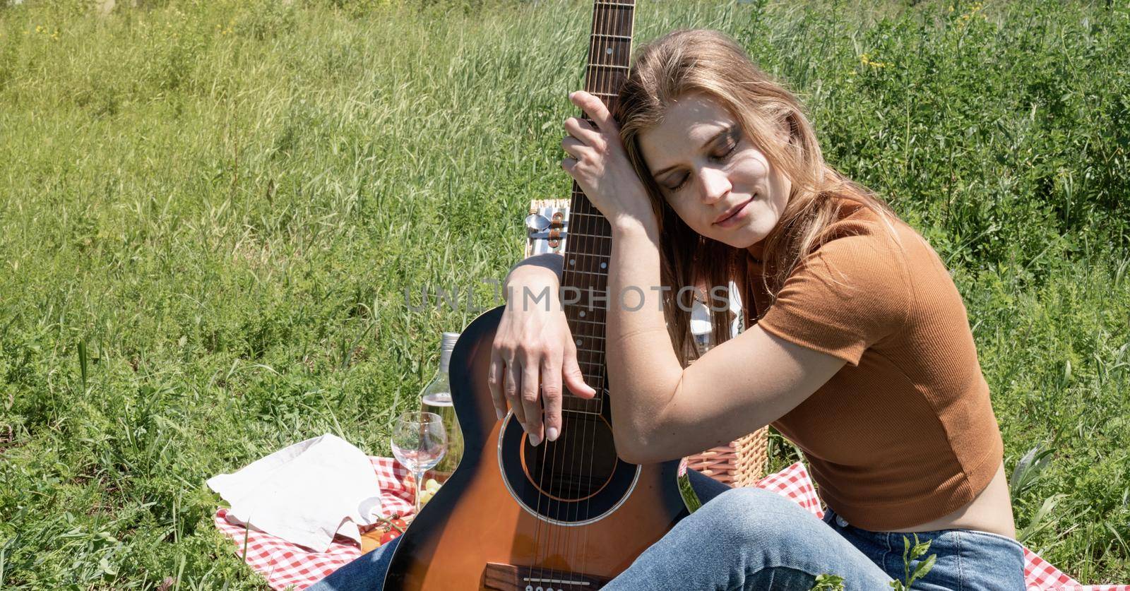 millennial woman in summer clothes and sunglasses playing guitar on a picnic. Happy woman holding her guitar peacefully sitting on grass