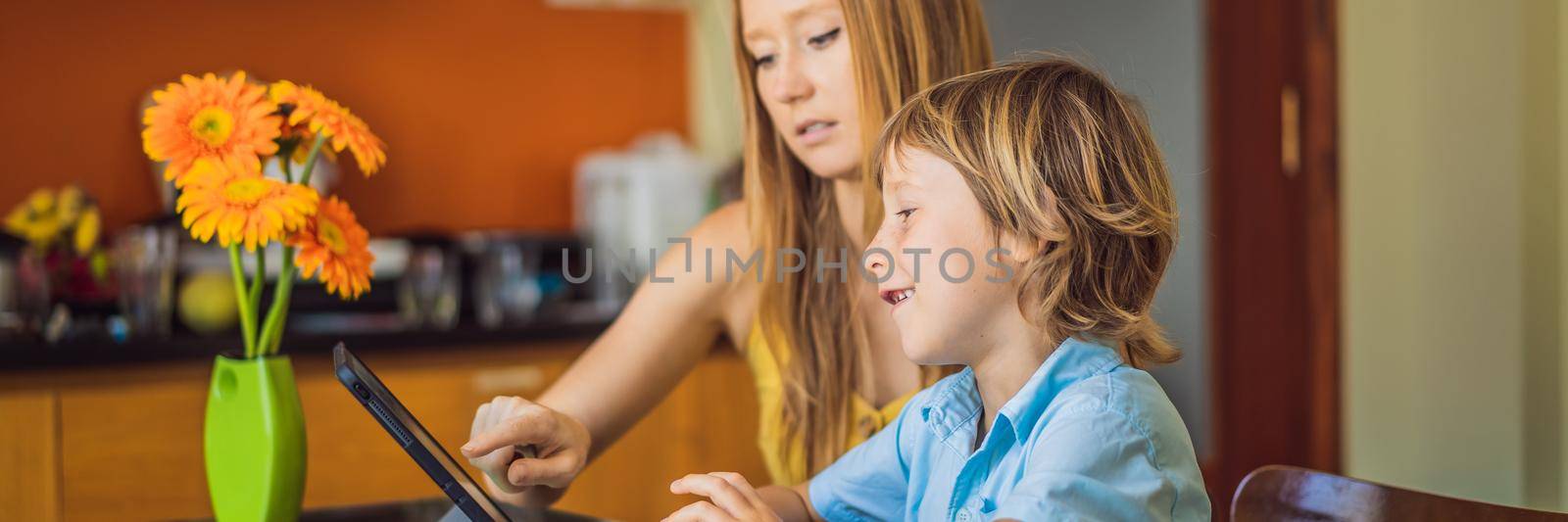 A boy studying online at home using a tablet. Mom helps him learn. Studying during quarantine. Global pandemic covid19 virus. BANNER, LONG FORMAT