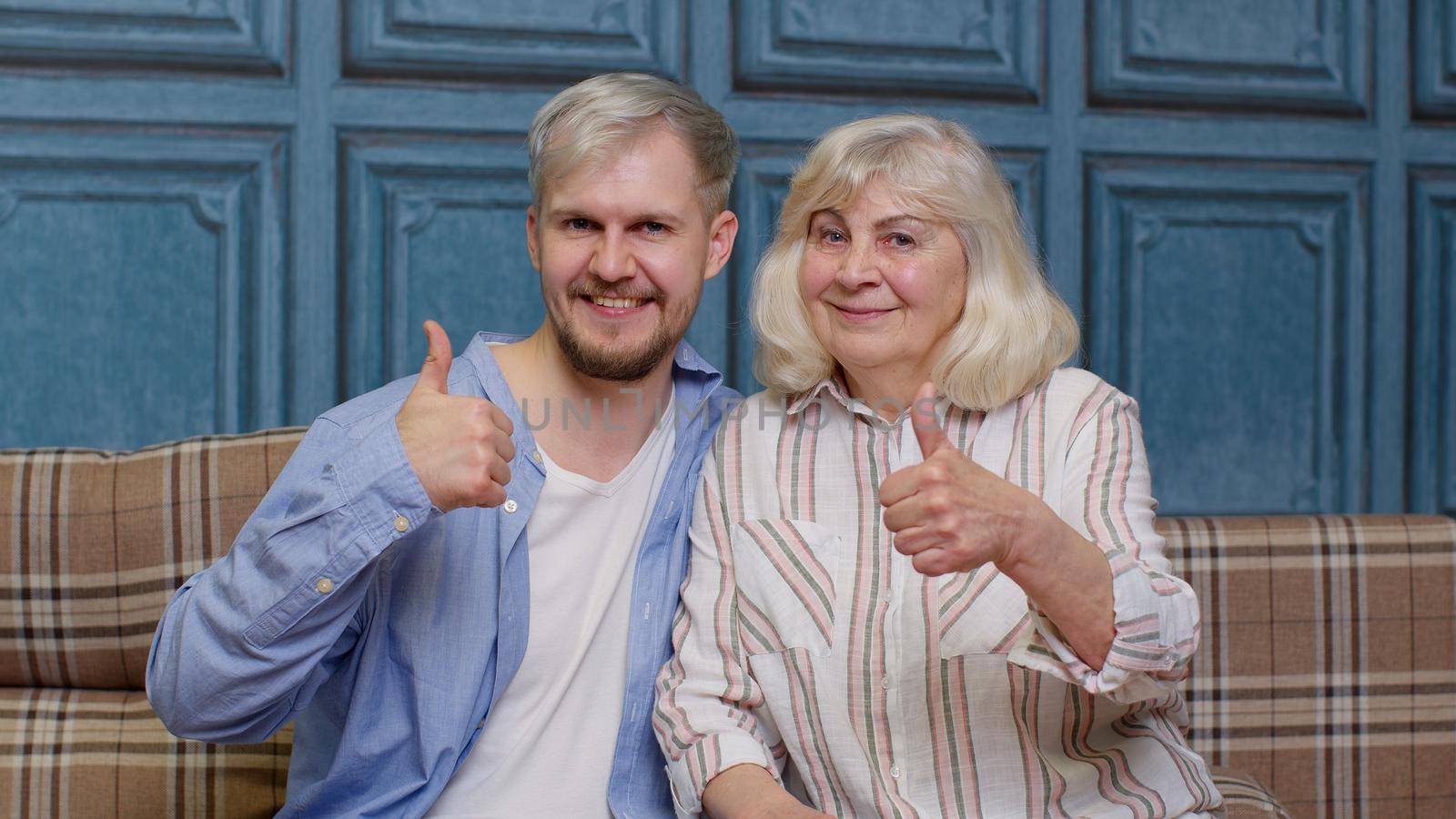 Joyful bonding loving generations family of senior mother and handsome adult son or grandson showing thumbs up gesture. Cheerful excited young man with gray-haired old mature mom or grandmother