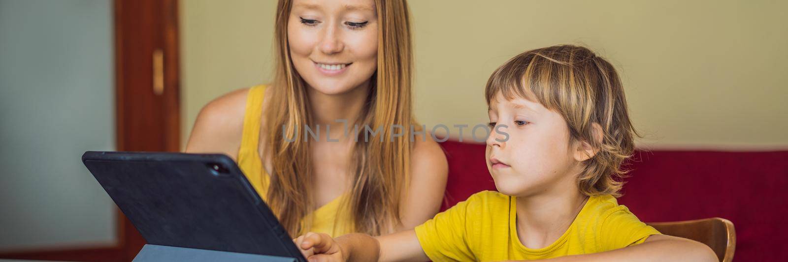 A boy studying online at home using a tablet. Mom helps him learn. Studying during quarantine. Global pandemic covid19 virus. BANNER, LONG FORMAT