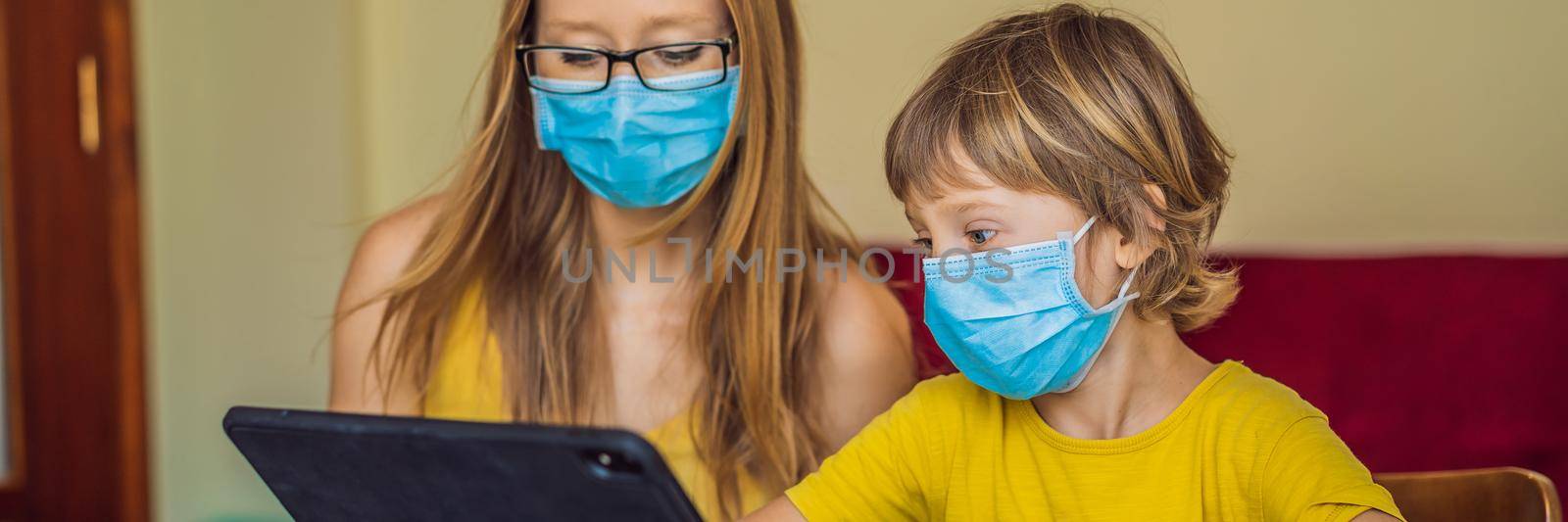 Boy studying online at home using a tablet. Mom helps him learn. Mom and son in medical masks to protect against coronovirus. Studying during quarantine. Global pandemic covid19 virus BANNER, LONG by galitskaya