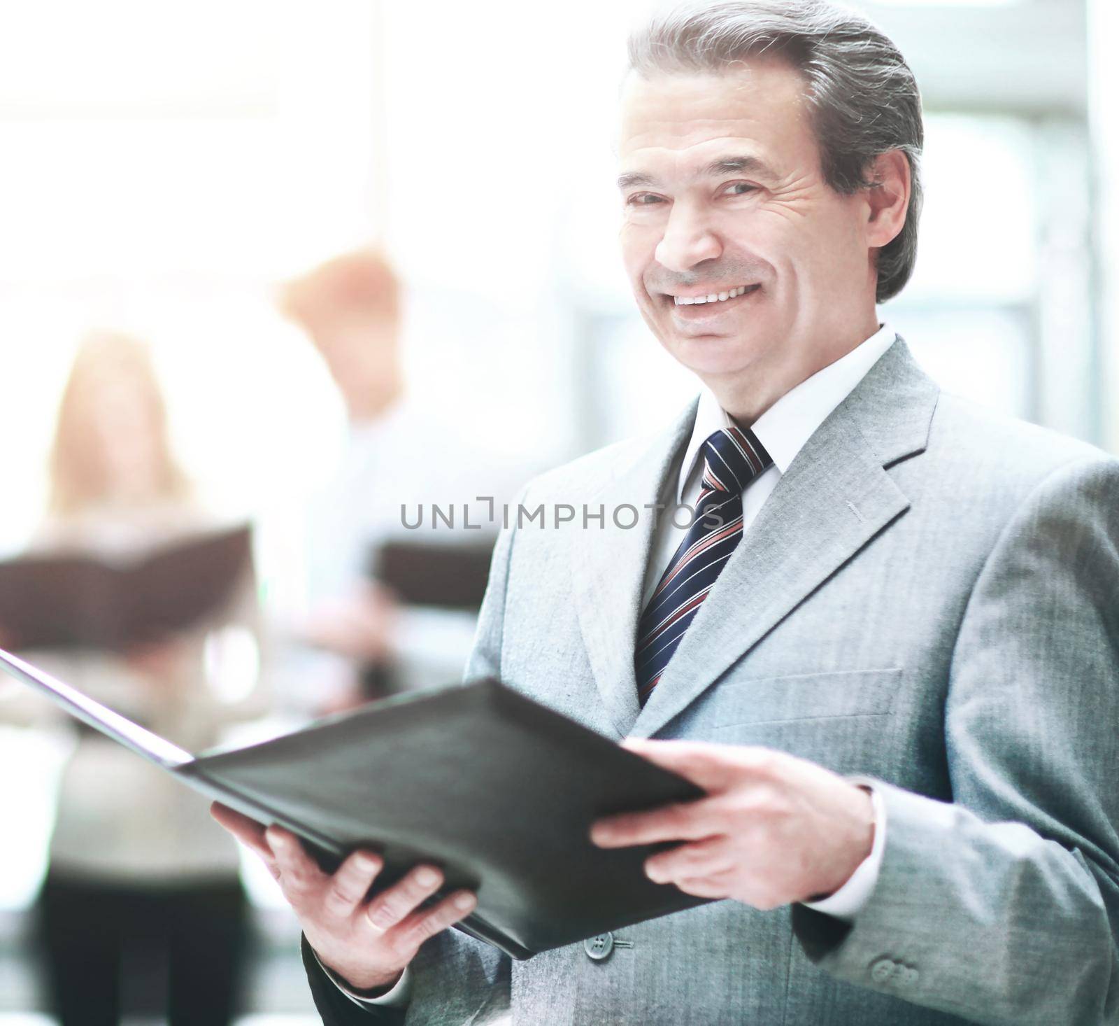 Successful business man standing with his staff in background at office