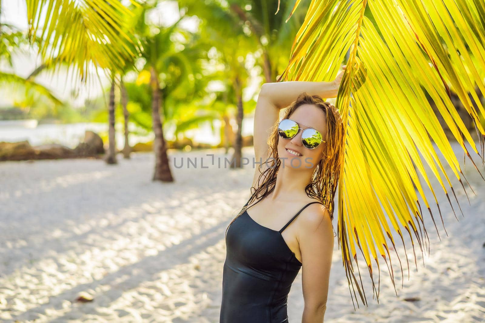 young beautiful woman in swimsuit on tropical beach, summer vacation, palm tree leaf, tanned skin, sand, smiling, happy. Happy traveller woman.