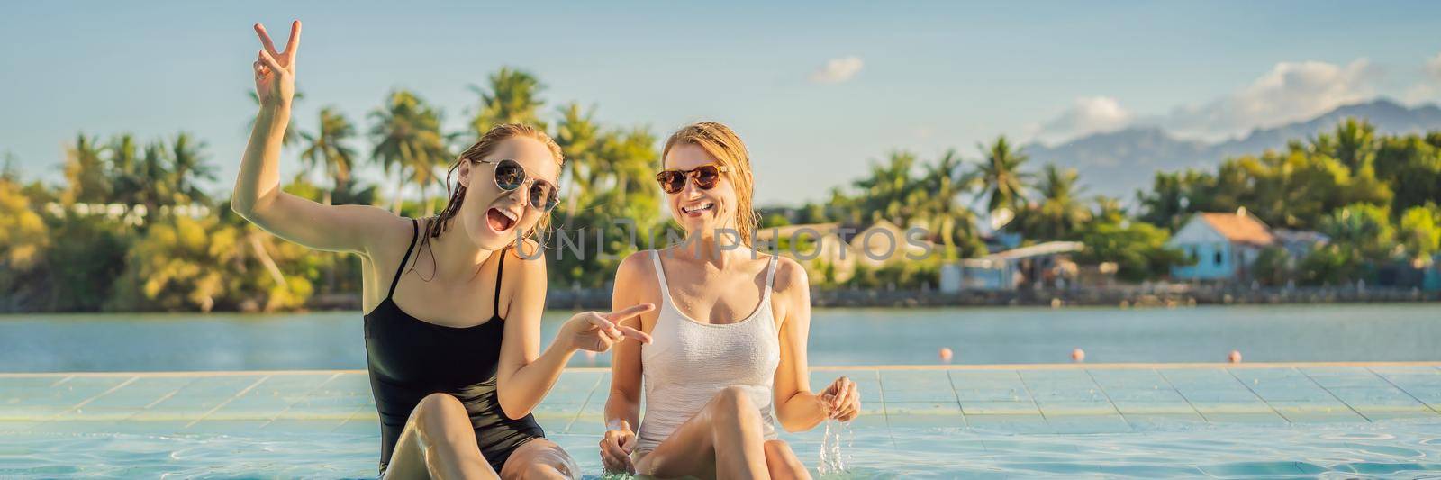 Two beautiful young woman sitting by the poolside of a resort swimming pool during summer holiday. Party, tourism in tropical countries BANNER, LONG FORMAT by galitskaya