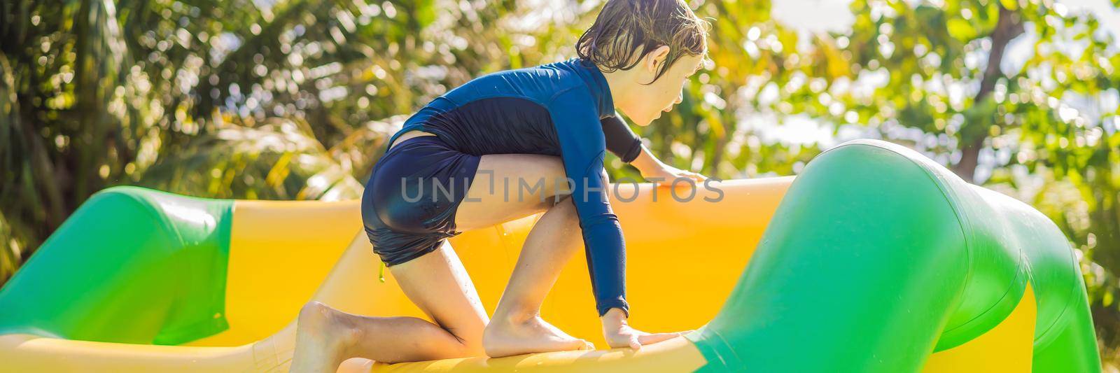 Cute boy runs an inflatable obstacle course in the pool BANNER, LONG FORMAT by galitskaya