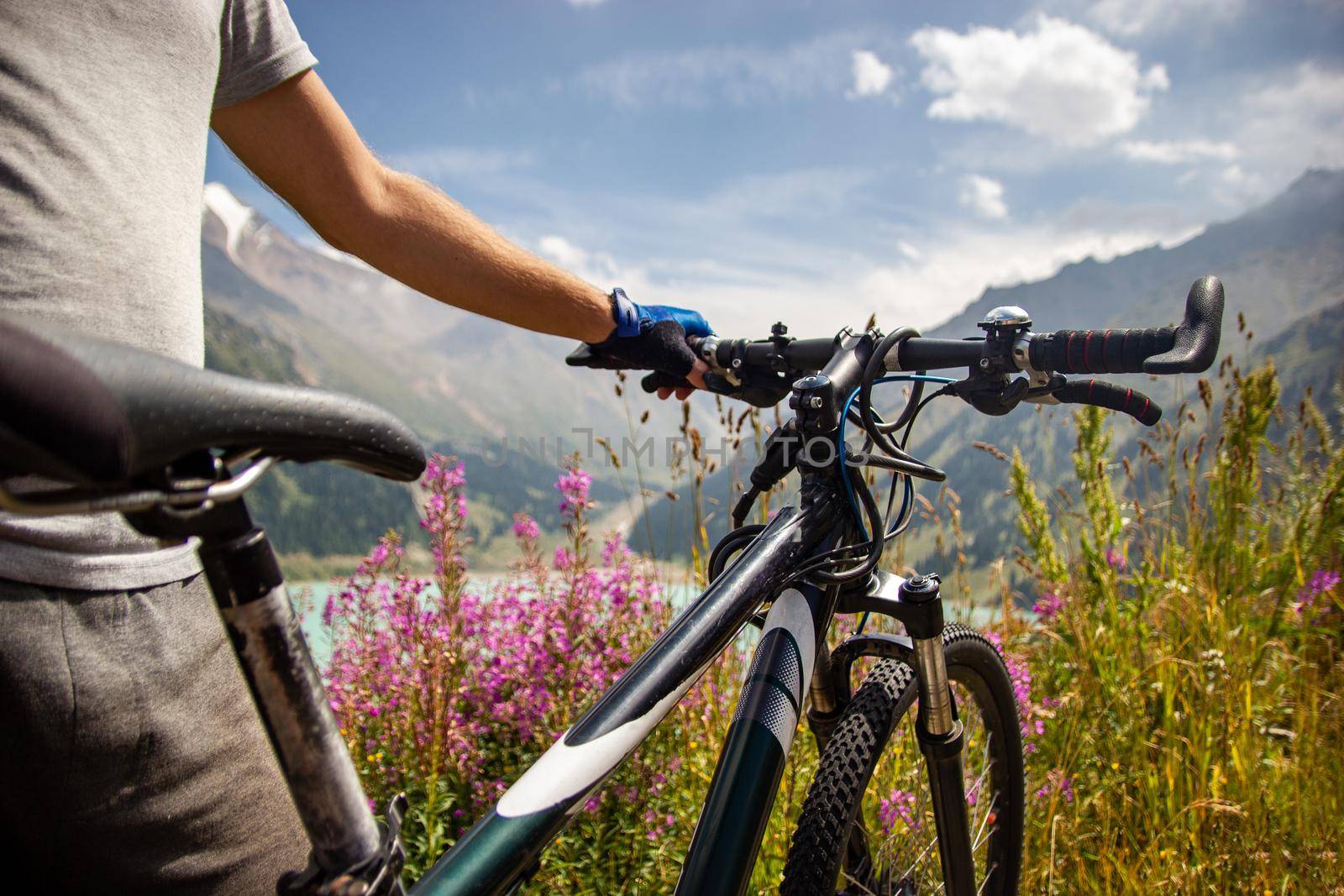 A man stands next to a mountain bike on the background of a mountain lake.