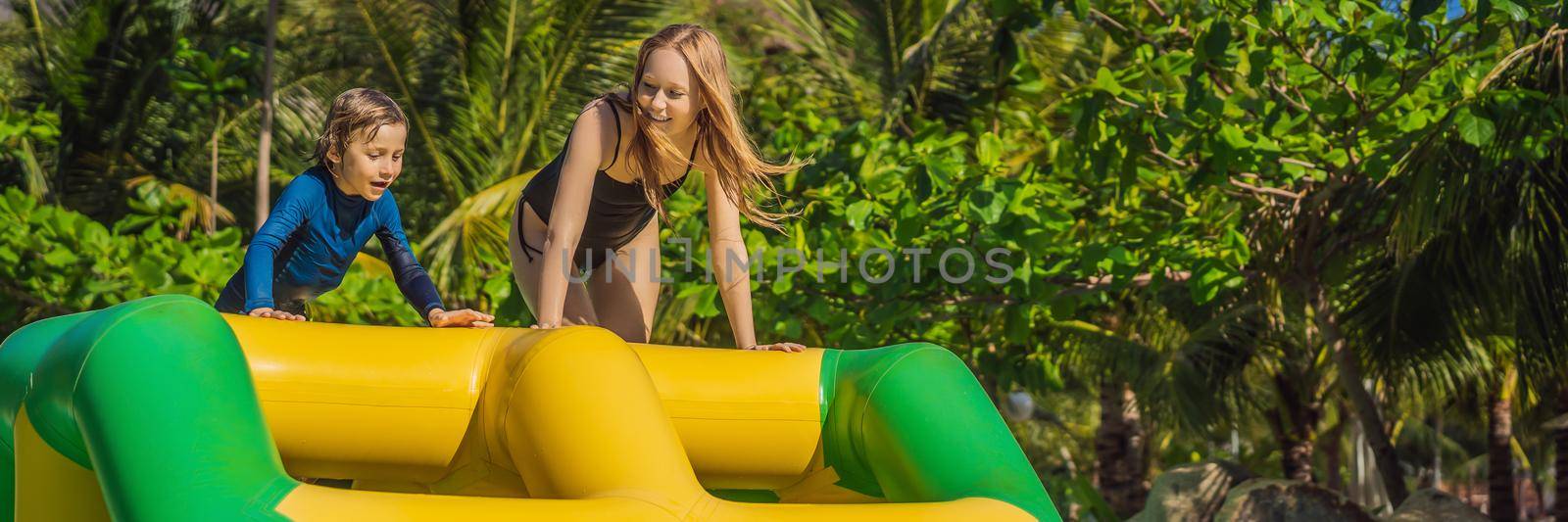Mother and son go through an inflatable obstacle course in the pool. BANNER, LONG FORMAT