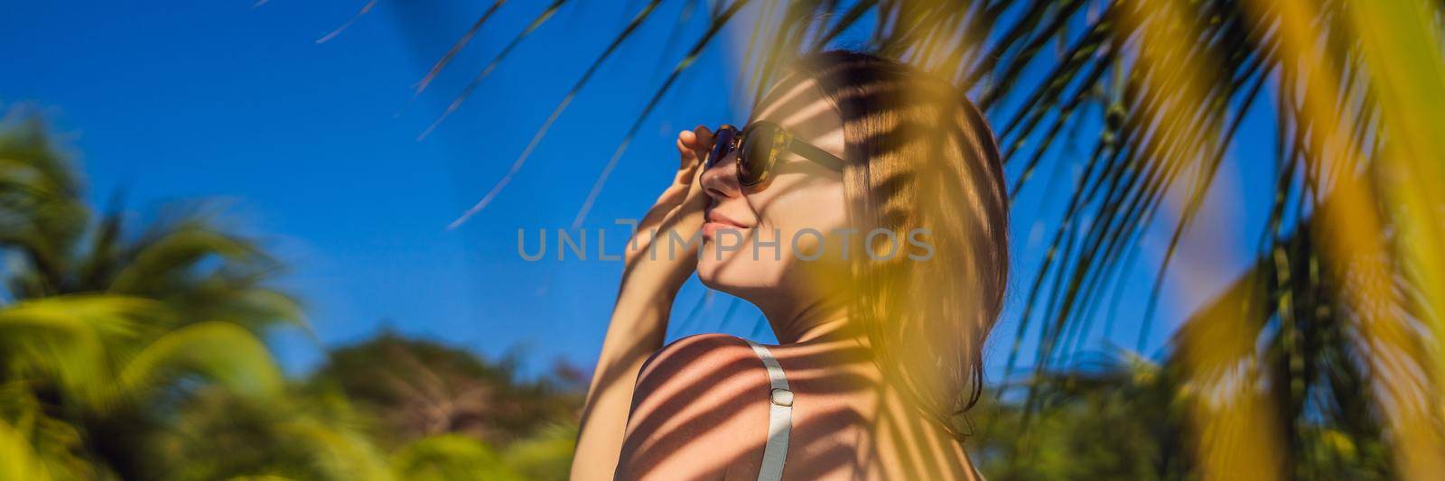 Young woman with the shadow of the palm leaf on her back. Relaxing on the seaside. BANNER, LONG FORMAT
