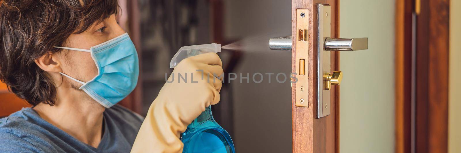 Coronovirus Prevention A man disinfects a doorknob. Closeup of a caucasian man disinfecting the door handle by spraying sanitizer from a bottle BANNER, LONG FORMAT by galitskaya