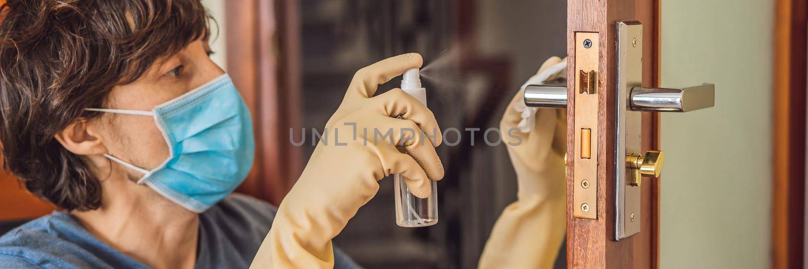 Coronovirus Prevention A man disinfects a doorknob. Closeup of a caucasian man disinfecting the door handle by spraying sanitizer from a bottle. BANNER, LONG FORMAT