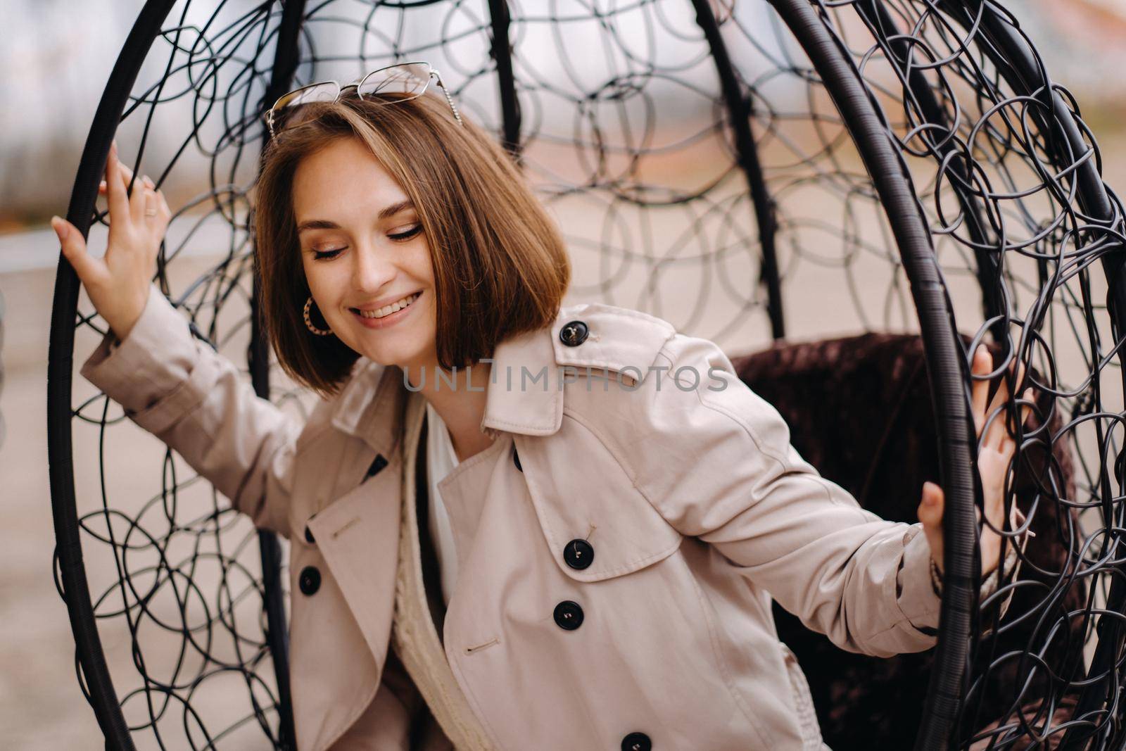 A happy stylish girl In a gray coat is sitting outside in an armchair.