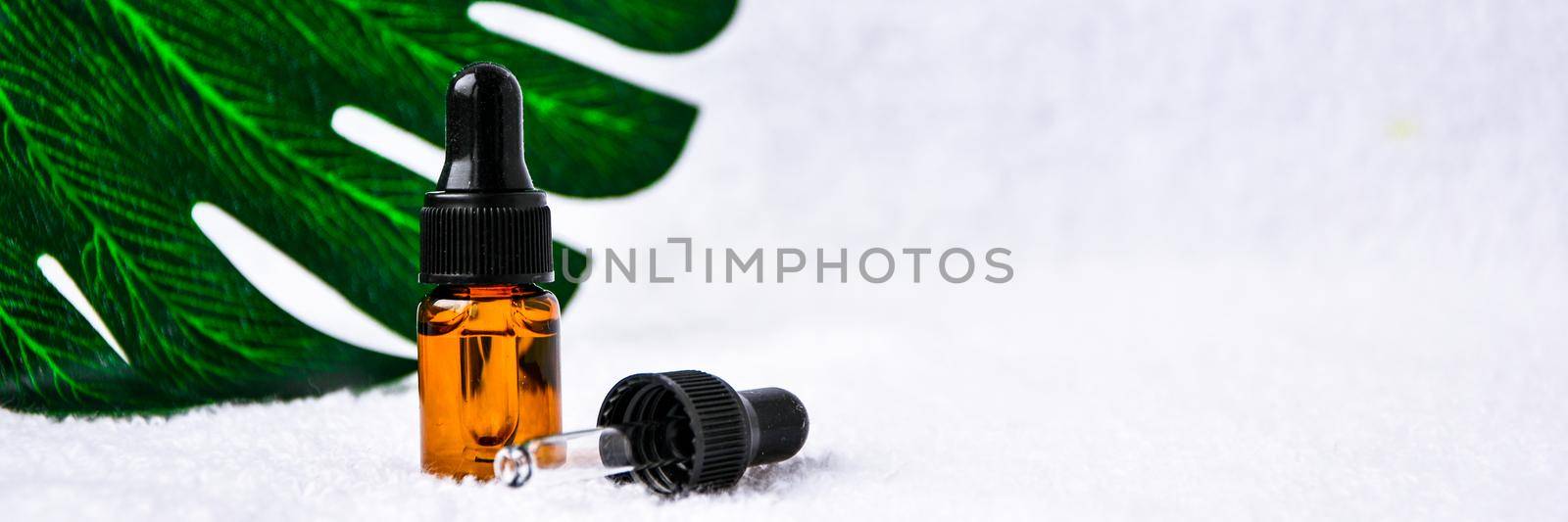 Dropper glass bottle skincare essential oil product for mock up in minimal style on white background with monstera leaf. Copy space. Blank aromatic oil container design, medical packaging template. Herbal cosmetic concept.