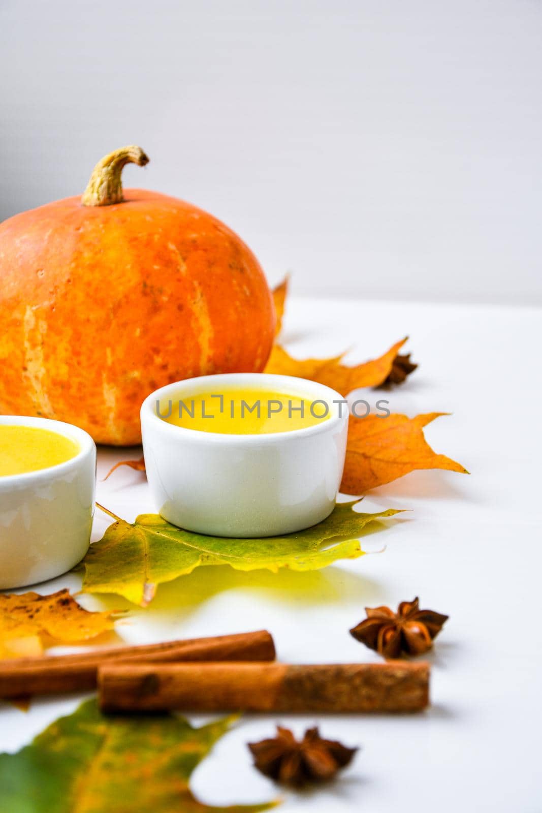 Autumn food. Pumpkin puree soup, leaves. Autumn harvest, pumpkins, leaves on grey as abstract background. Thanksgiving day. Seasonal food. Vegetarian