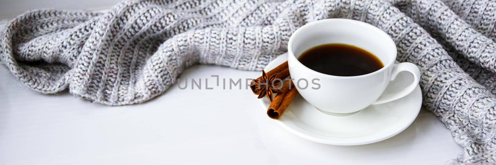 Cup of coffee with cinnamon sticks and anise star on white background. Sweater around. Winter morning routine. Coffee break. Copy space. by anna_stasiia