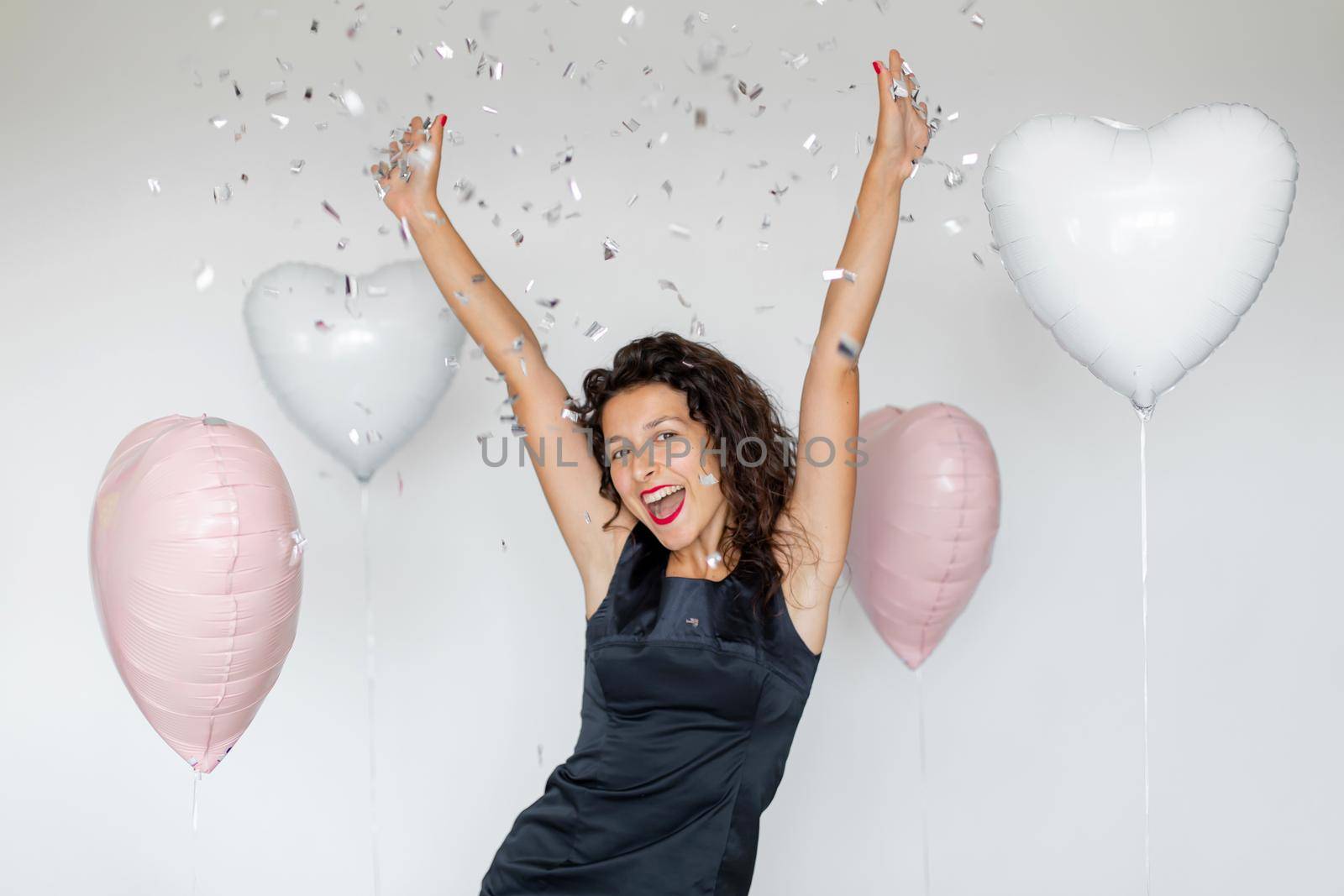 The emotion of success. Happy sexy brunette girl enjoying celebrating with confetti and heart balloons on a white background.