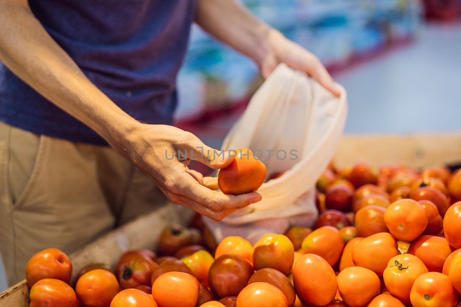 Man chooses tomatoes in a supermarket without using a plastic bag. Reusable bag for buying vegetables. Zero waste concept by galitskaya